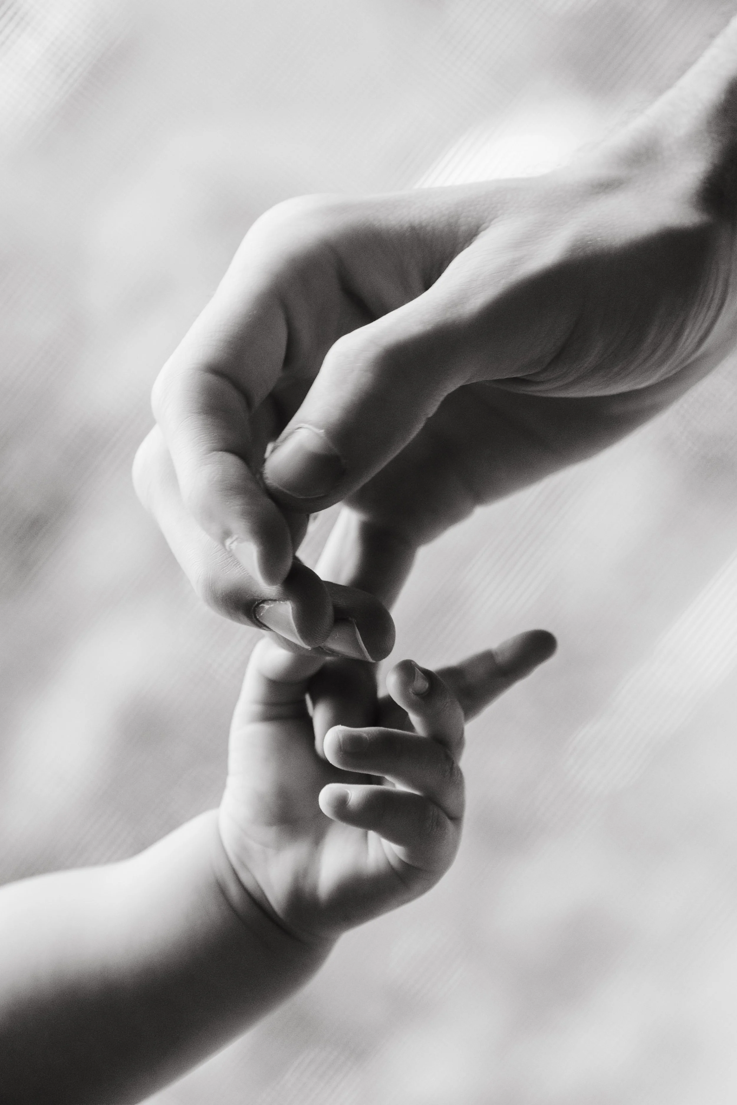 A black and white photo of a parent gently holding a child's smaller hand, with the child's finger pointing upward, in Brooklyn by Maison Mancel.
