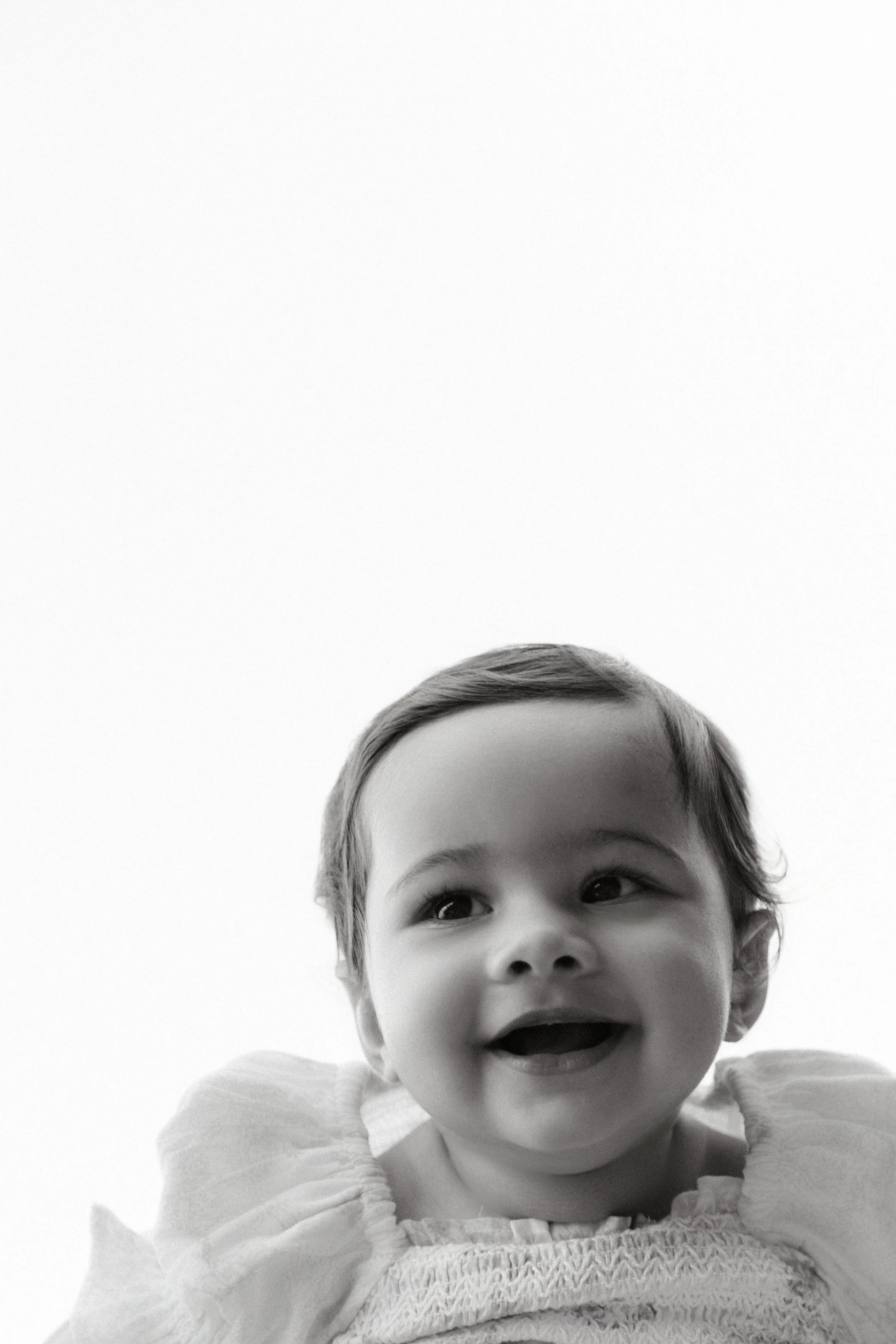 Black and white lifestyle family photo of a smiling toddler girl with short hair, looking up and to the side, wearing a ruffled top in Brooklyn, by Maison Mancel.