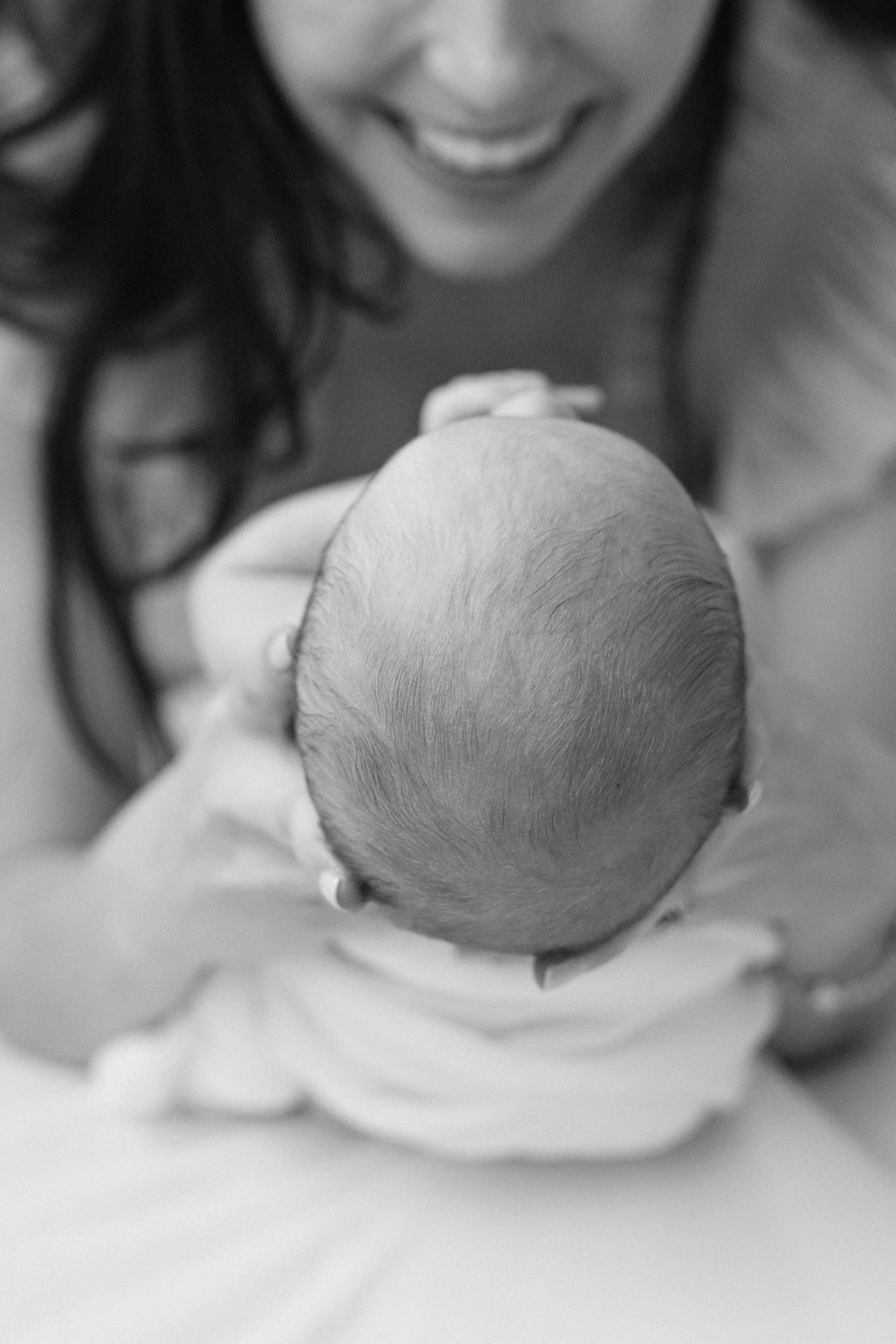 A smiling mother holding a newborn baby in her arms, viewed from above, in black and white, photographed by Maison Mancel in-home in NYC.