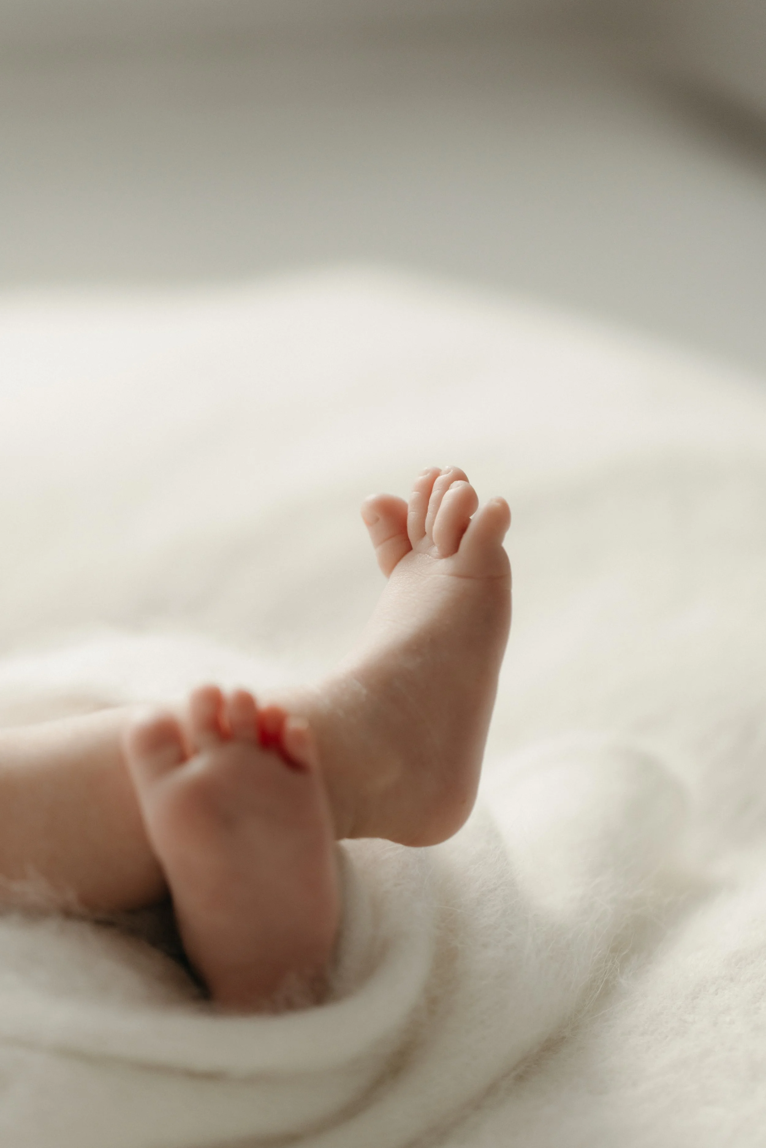 Close-up of a baby's foot resting on a soft, white surface with a neutral background, photographed by Maison Mancel in NYC.