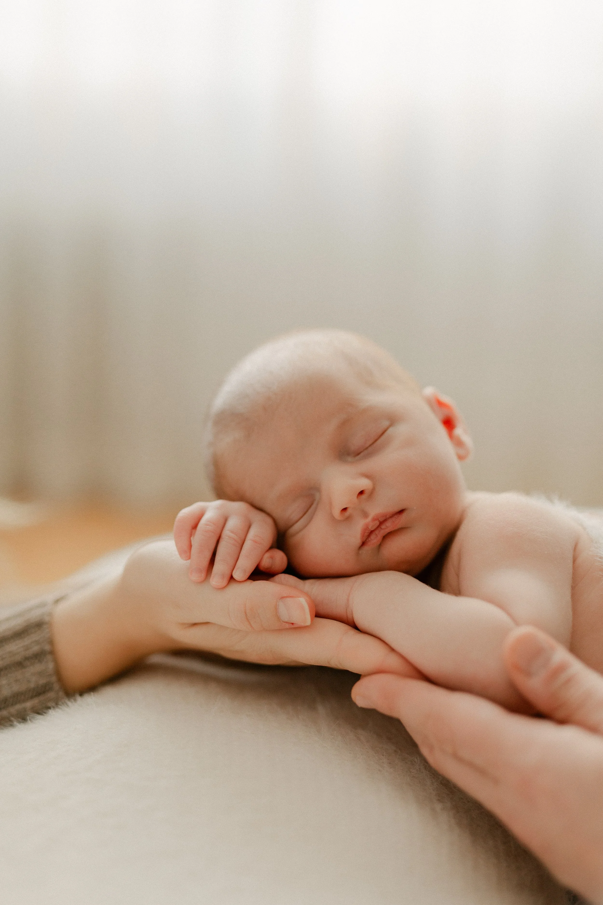 A newborn portrait featuring a sleeping newborn baby lying on a person's arm and shoulder, with eyes closed and peaceful expression. Photographed by Maison Mancel in NYC home in TriBeCa.