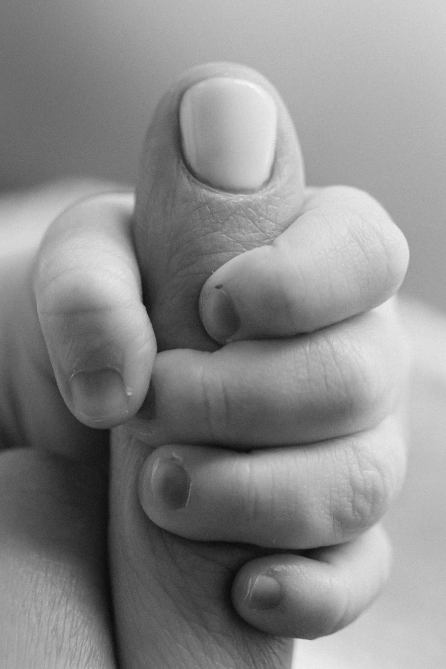 Close-up black and white photo of a small newborn hand gripping an adult finger, photographed by Maison Mancel in NYC.