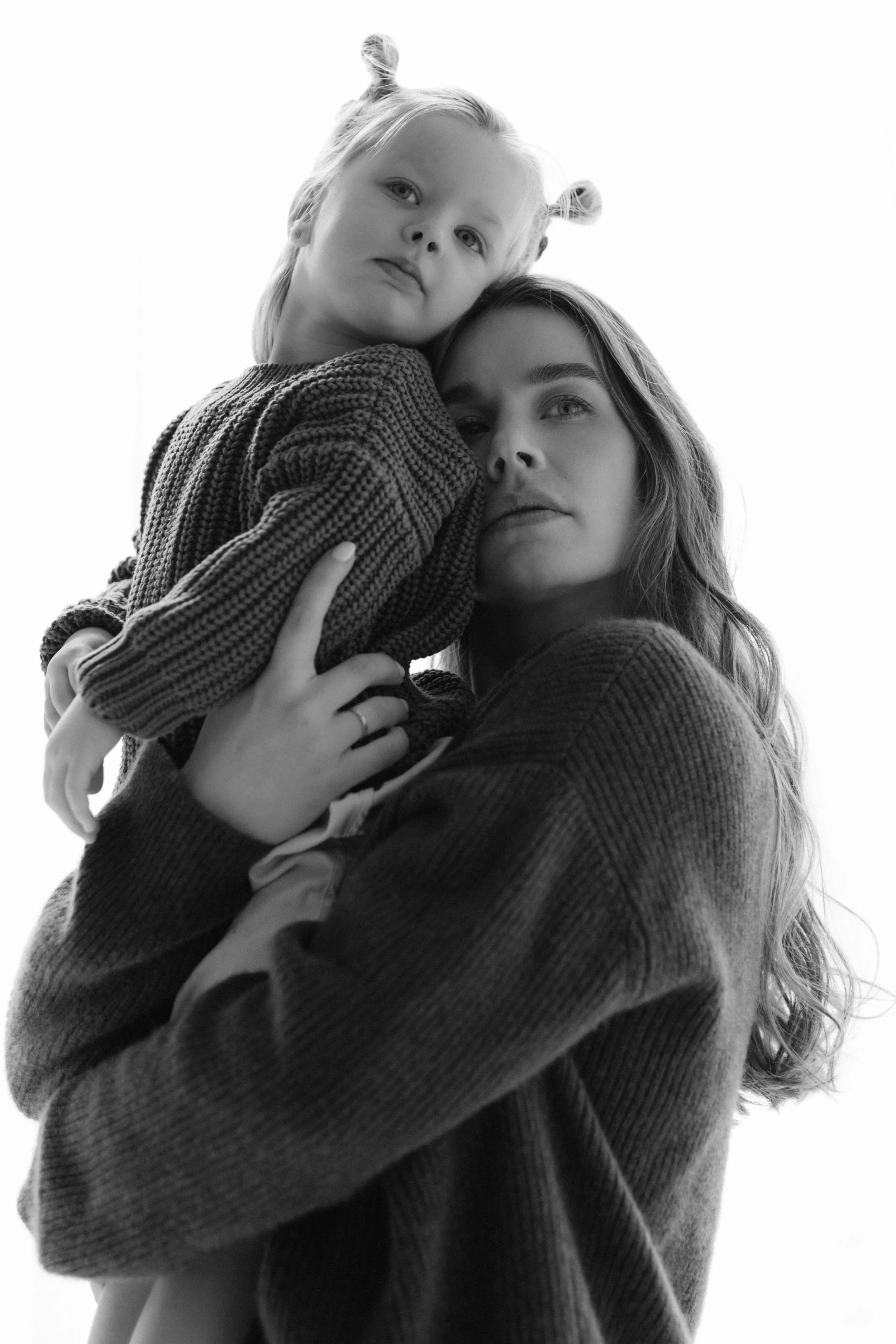 An in-studio portrait of a mother  holding a young girl, both looking at the camera, against a bright background, by Maison Mancel in NYC.