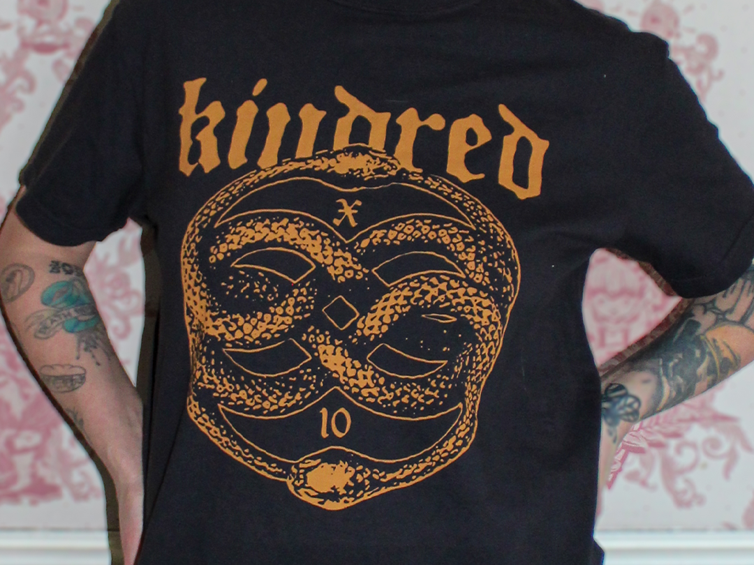 A person wearing a black t-shirt with orange graphic design and text that says "killed" at the top. The design features a snake coiled into the shape of an infinity symbol with the number "10" below it.
