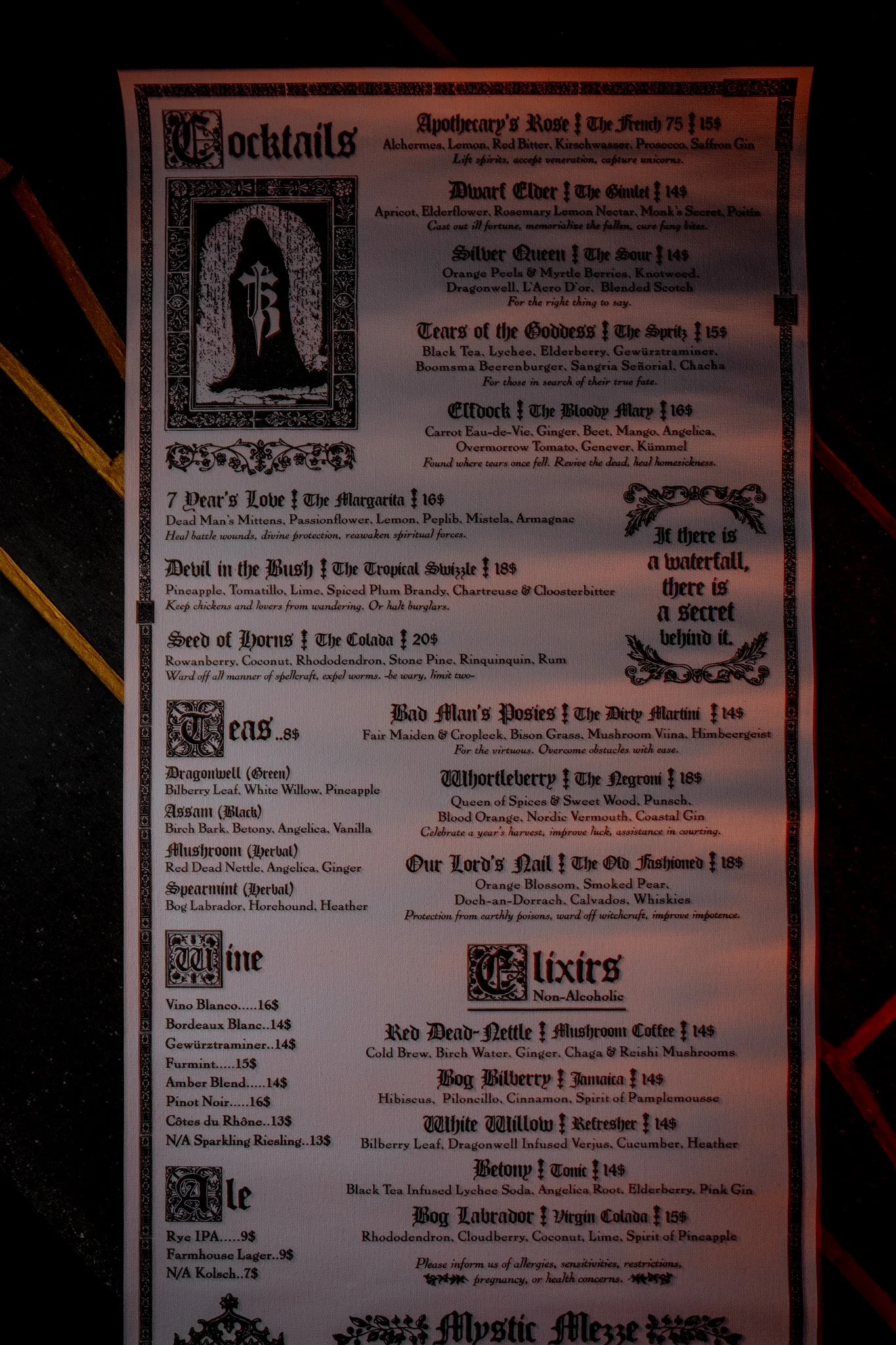 A menu from a themed bar or restaurant featuring gothic-style decorative borders, dark text, and a silhouette illustration of a woman with a sword on the left side. The menu lists various cocktails, wines, and other beverages with descriptions and prices.