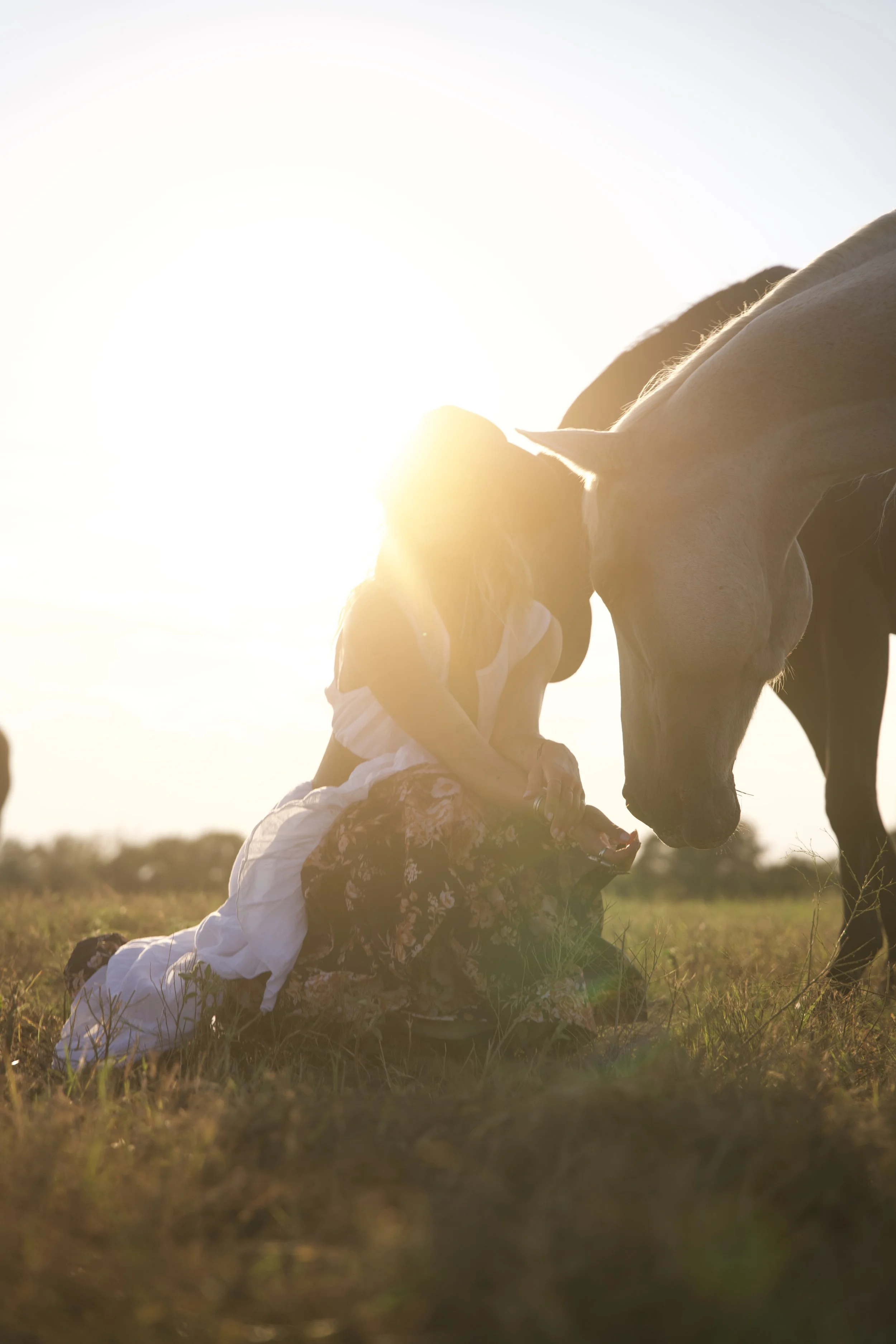 A woman in a white dress kneeling in a pasture at sunset at Stardust Ranch in Round Top, Texas, photographed to promote experiential travel, ranch events, and destination marketing initiatives.