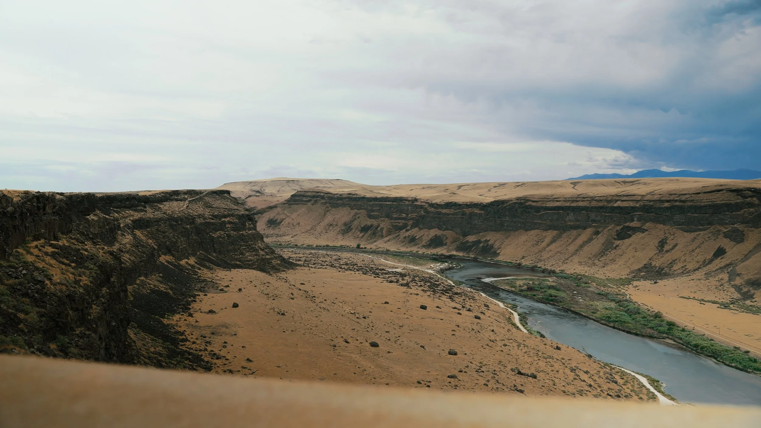 A vast desert landscape with steep canyon walls and a winding river flowing through the valley.