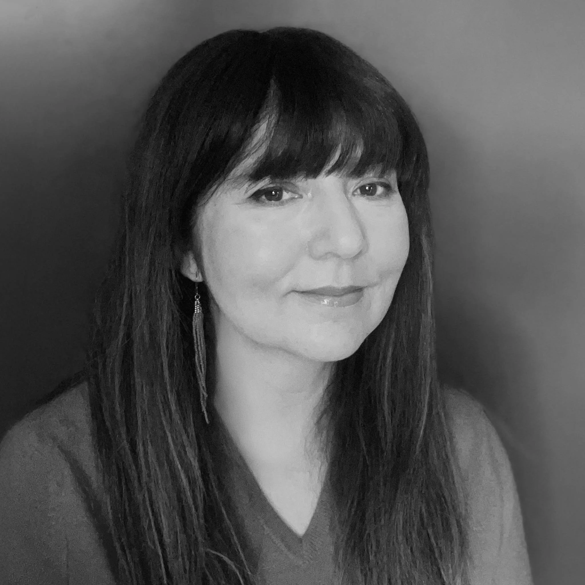Black and white portrait of a woman with long hair and bangs, wearing earrings.