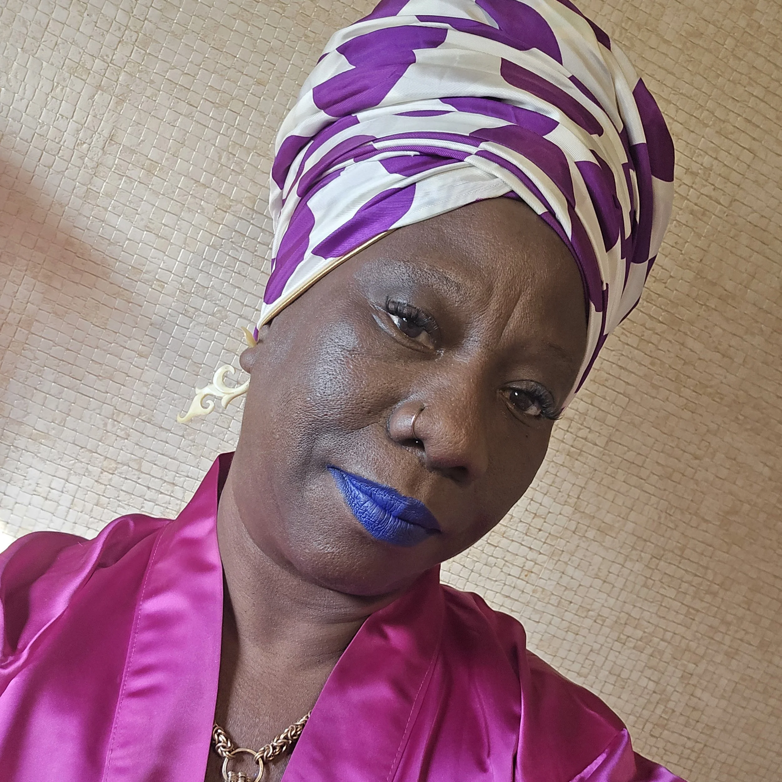 Person wearing a purple and white headscarf and vibrant blue lipstick, dressed in a purple robe.