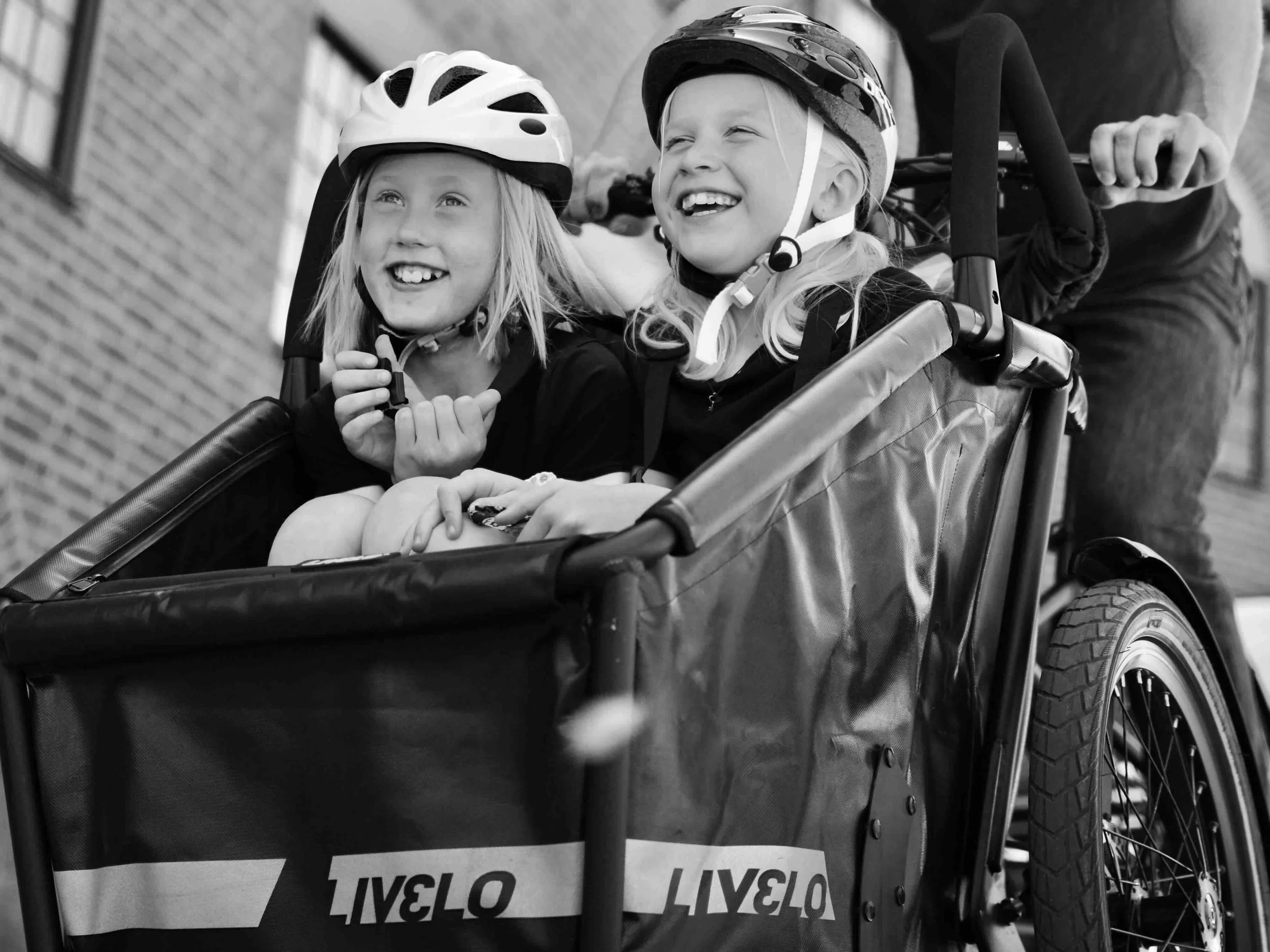 Två glada tjejer sitter i korgen på en Livelo el-lådcykel.