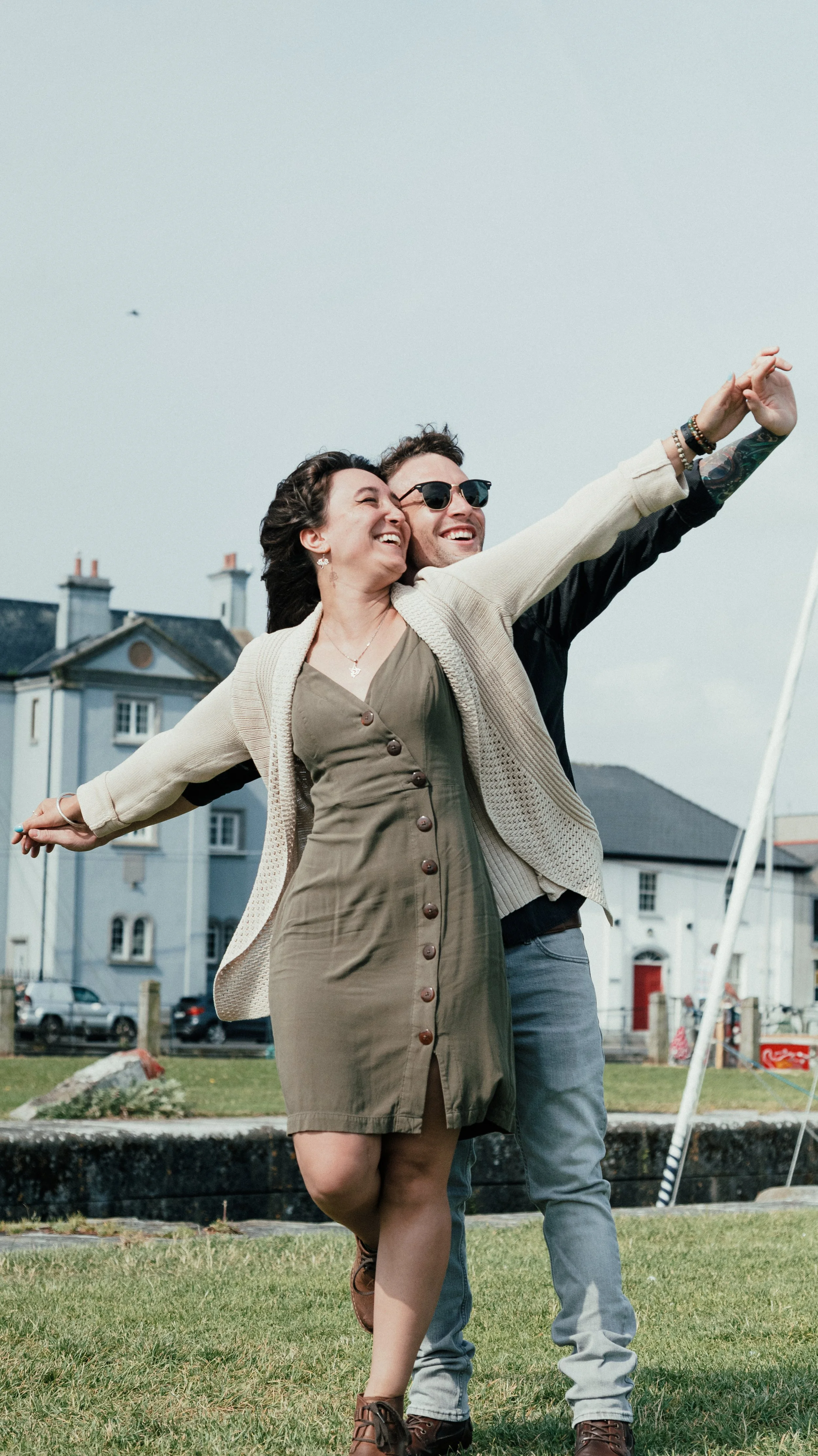 A happy couple dancing and laughing outdoors on a grassy area with houses in the background.