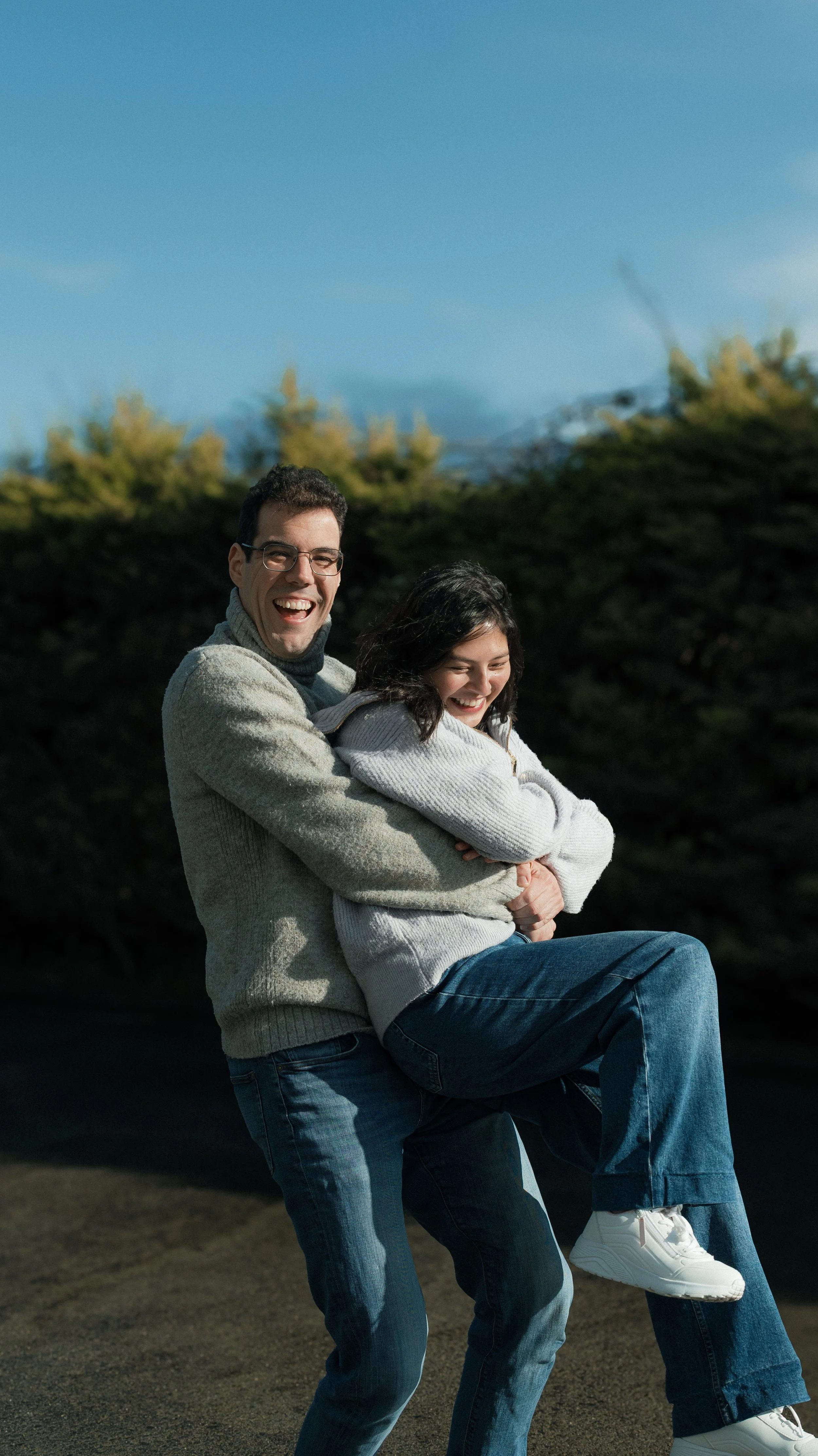 A smiling man and woman enjoying a playful moment outdoors, with the man holding the woman in his arms.