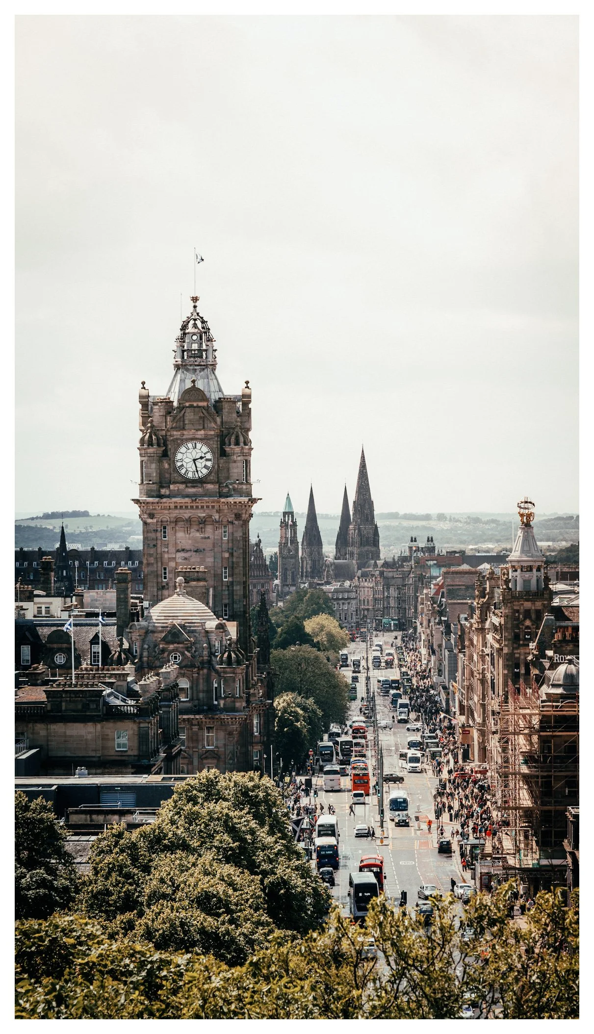 A cityscape showing a busy street with cars and buses, a historic clock tower, and several church spires in the background.