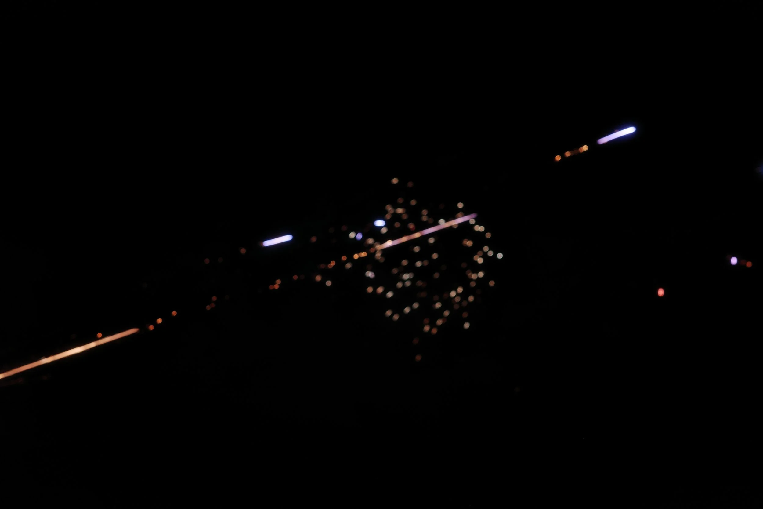 Nighttime aerial view of a city with illuminated streets and buildings, seen from an airplane window.