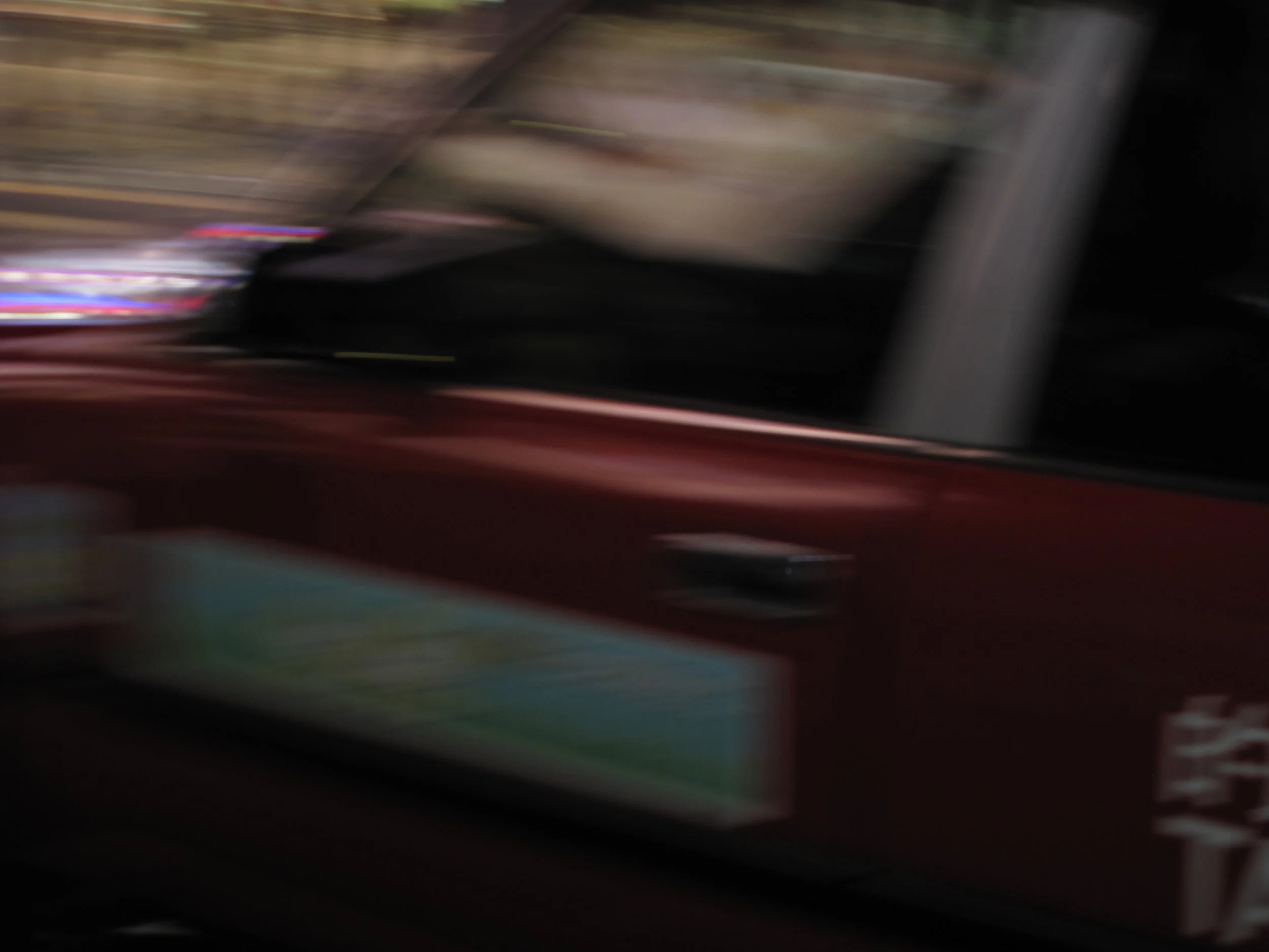 Blurred photo of a red vehicle with some signs and background lights visible.