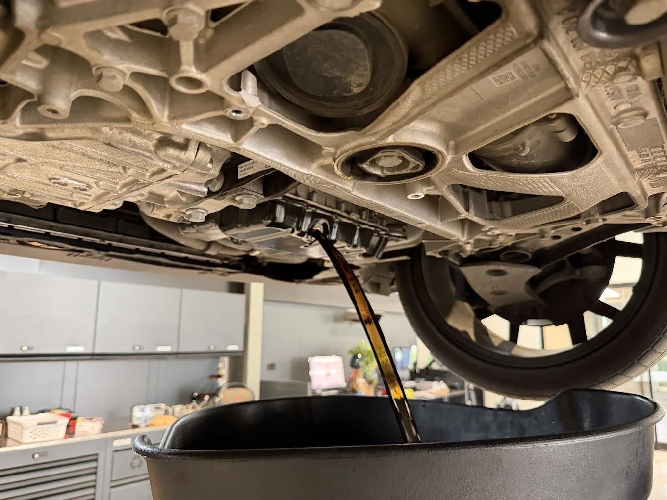 Automobile undercarriage with engine oil being drained into a black container.