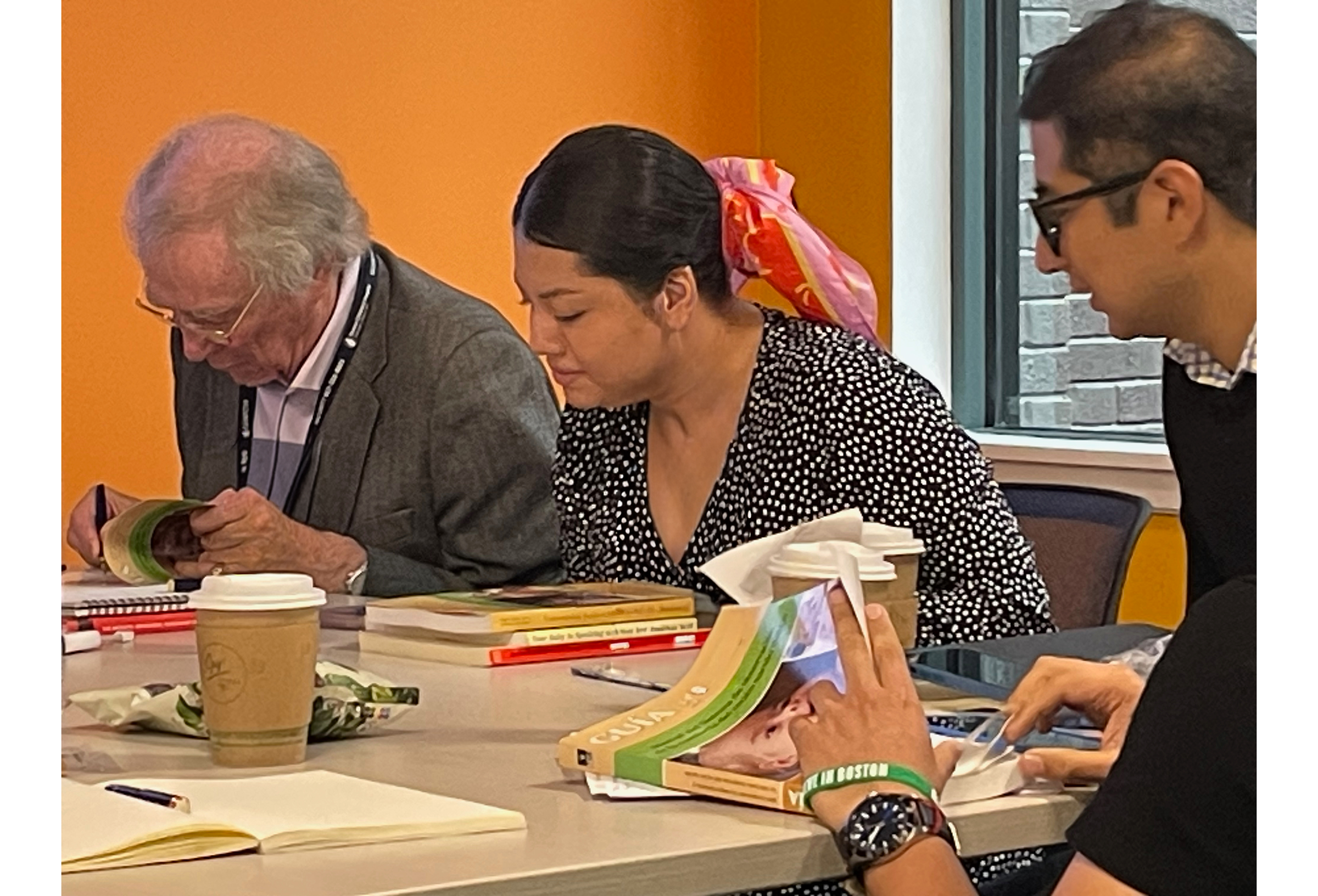 Practitioners seated at a table with Dr. Kevin Nugent reading and discussing books on newborn behavior, reflecting focused learning and collaboration during an early relational health training.