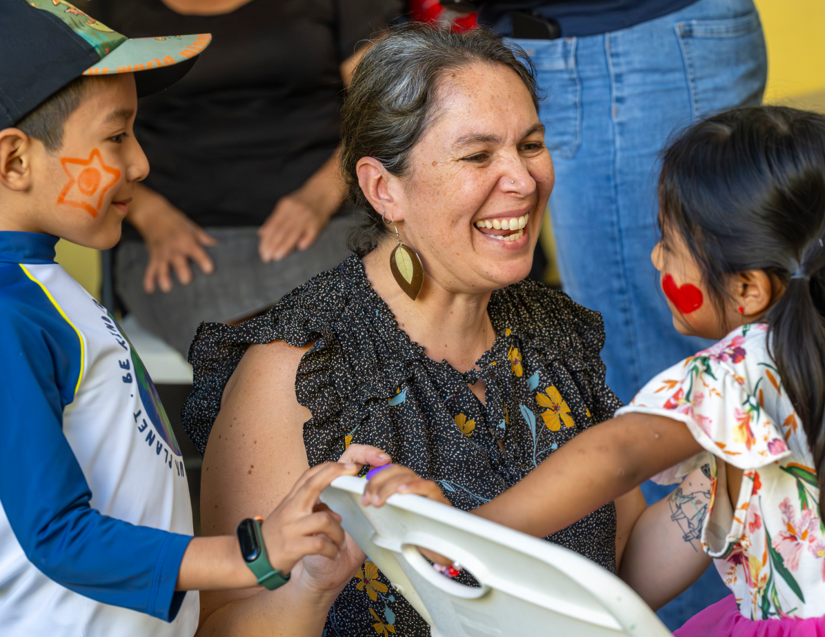 An adult smiling and engaging with children during a shared activity, reflecting an inclusive and welcoming environment centered on care and participation.