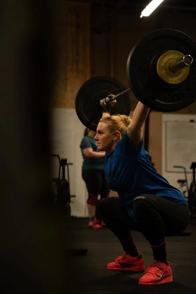 A woman lifting a barbell with weights overhead during a workout in a gym.