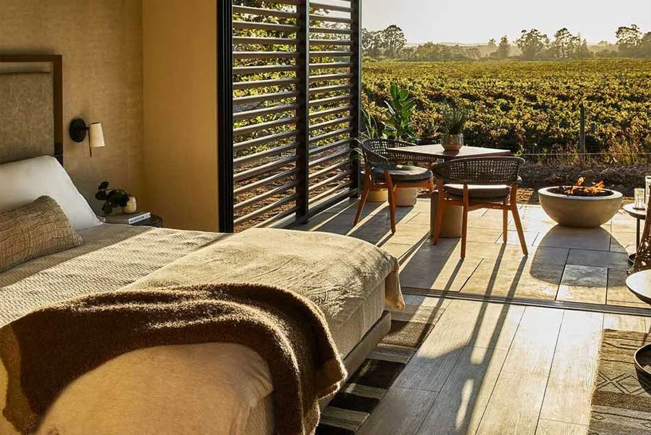 Late afternoon light filters into a hotel room at Stanly Ranch, across the vineyards outside onto a bed dressed in natural tones and linen.