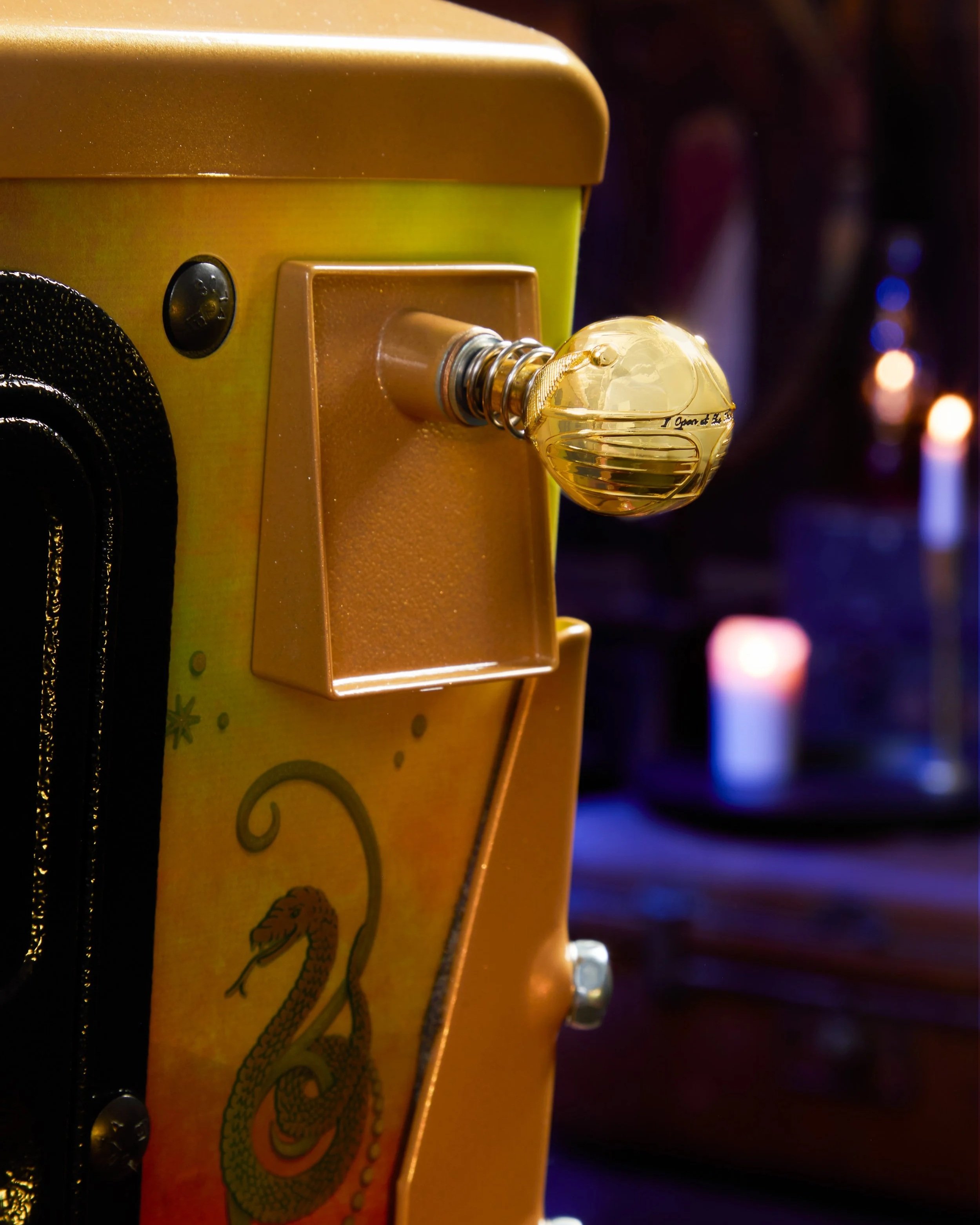 Close-up of a yellow and gold arcade game machine with a shiny spherical control knob and a partial dragon illustration on the side.