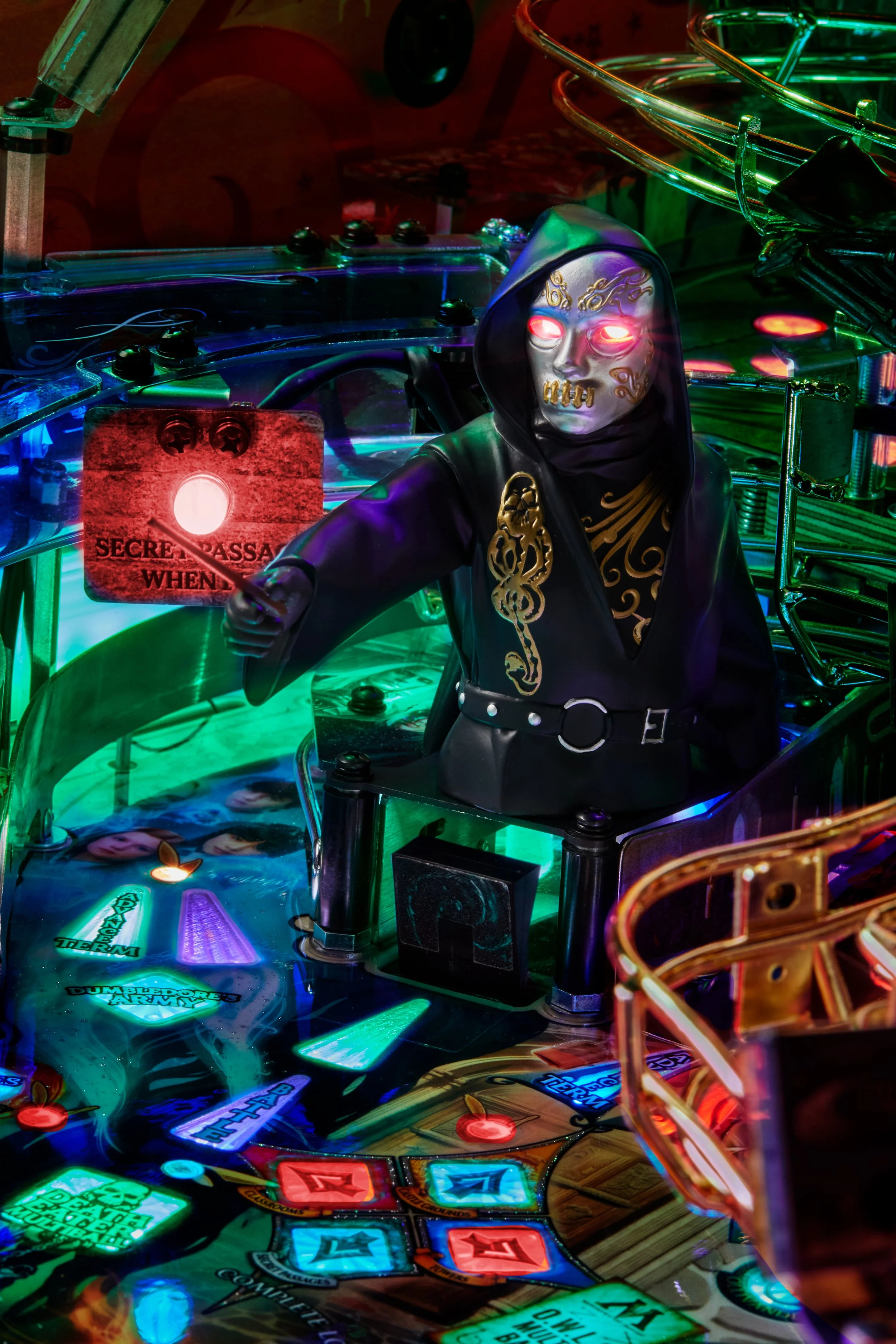 A pinball machine with a spooky, masked figure wearing a dark hooded cloak and gold designs on the face and clothing, surrounded by colorful lights and metallic ramps.