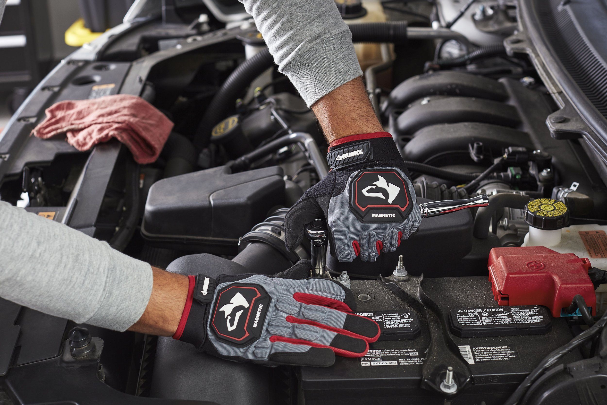 Person working on car engine, using a wrench and wearing Husky gloves, with a red cloth on the engine.
