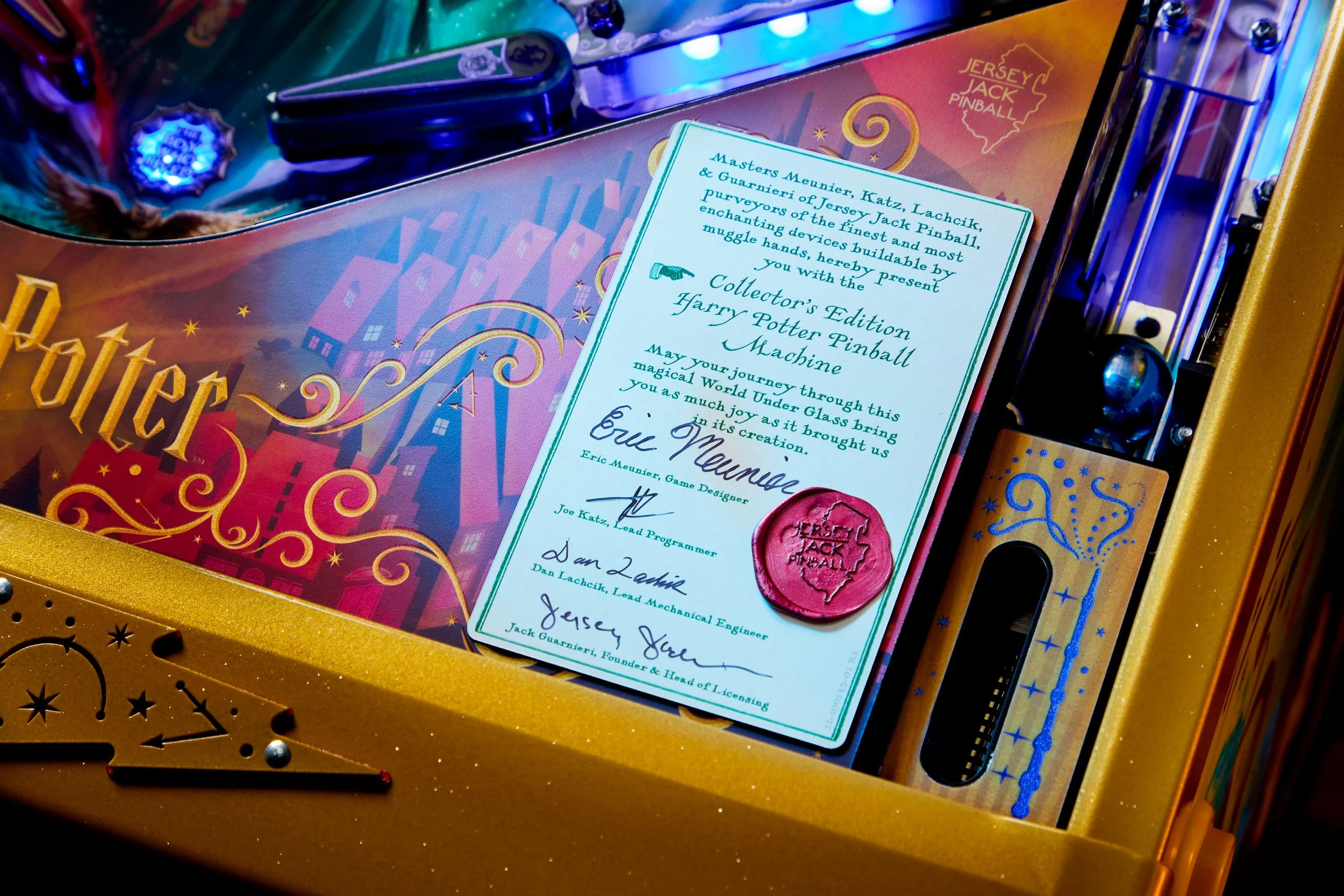 Close-up of a Harry Potter-themed pinball machine with a certificate of authenticity, featuring a red wax seal that says Jersey Jack Pinball, and a colorful backdrop with illustrations of wizarding themes.
