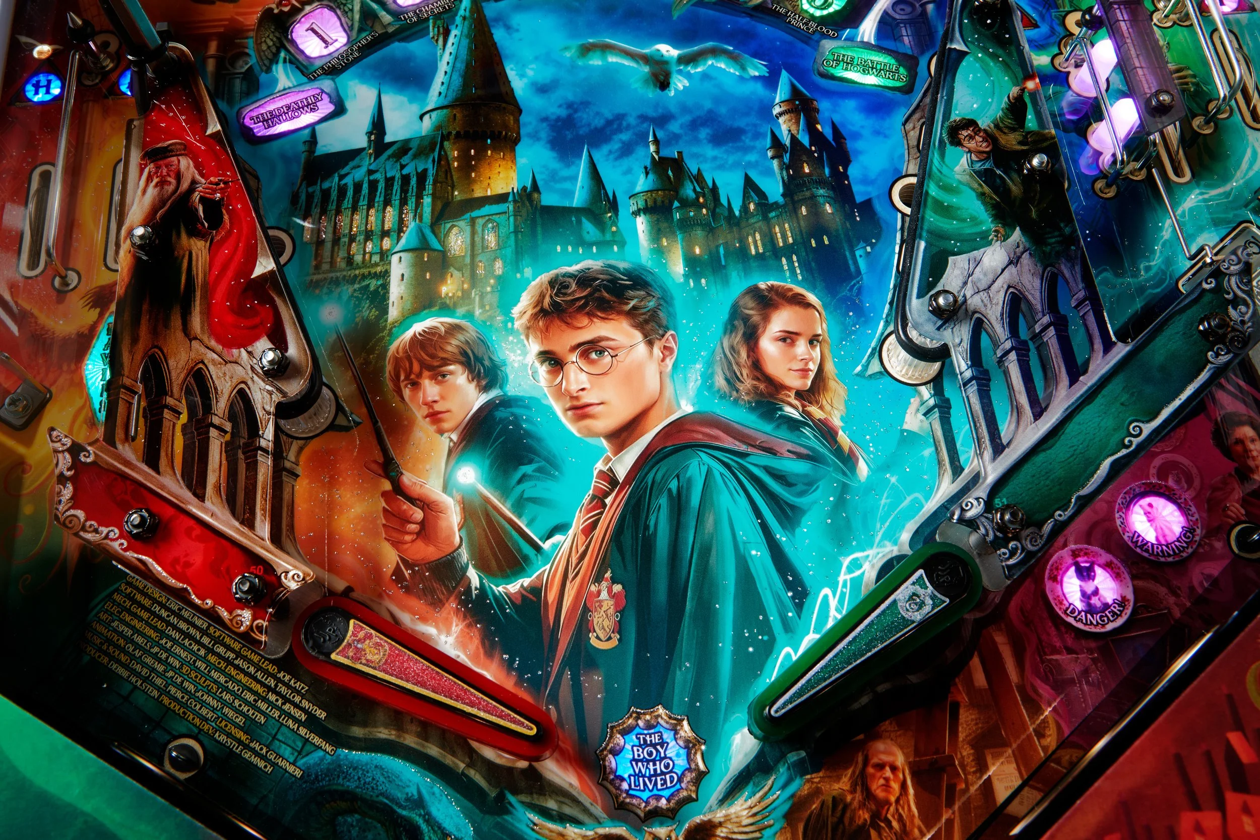 Close-up of a Harry Potter-themed pinball machine featuring characters Harry Potter, Ron Weasley, and Hermione Granger, with a castle in the background and various colorful lights and buttons.