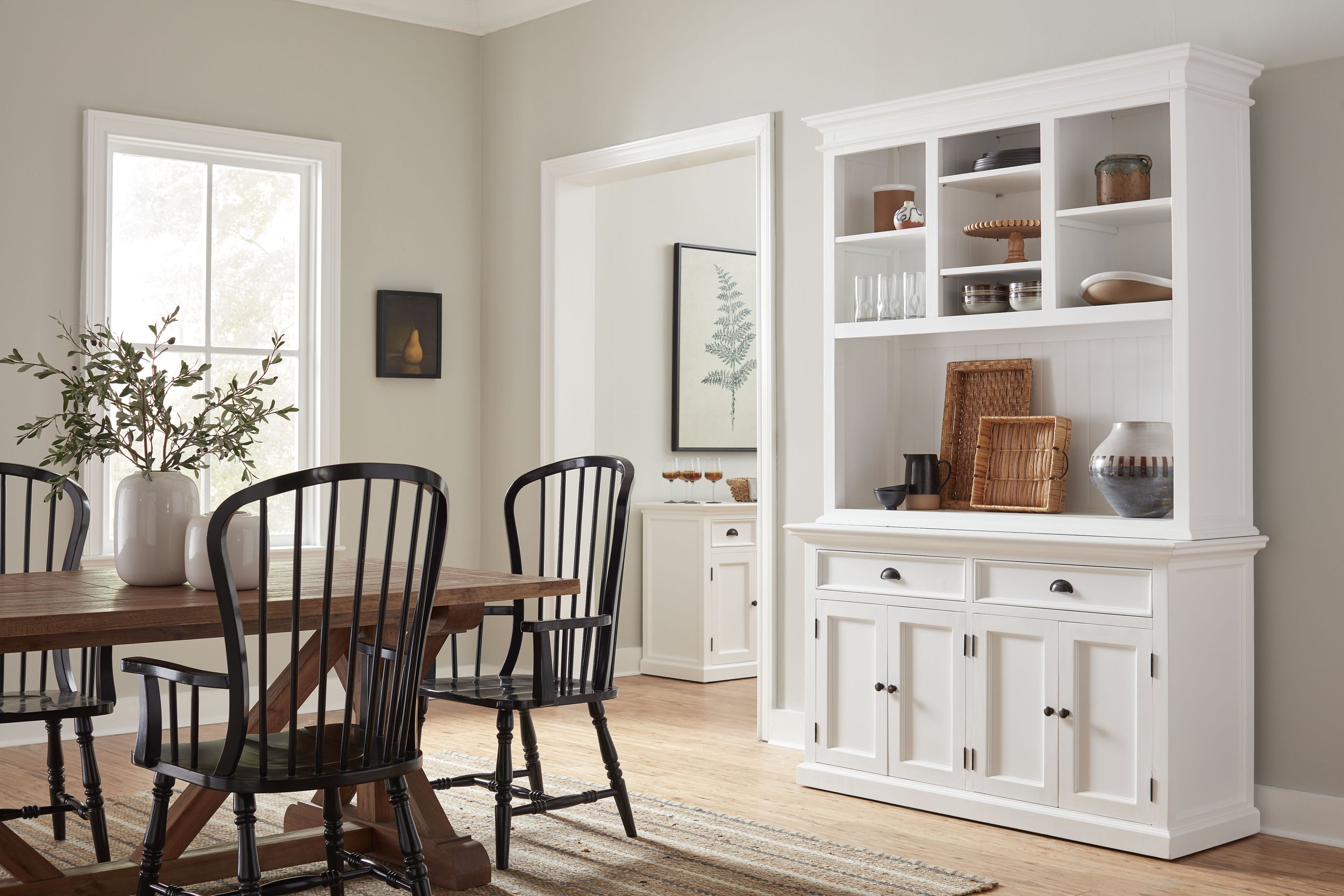 Dining room with a wooden table, black chairs, large window, white china cabinet with decorative items, and framed artwork on the wall.