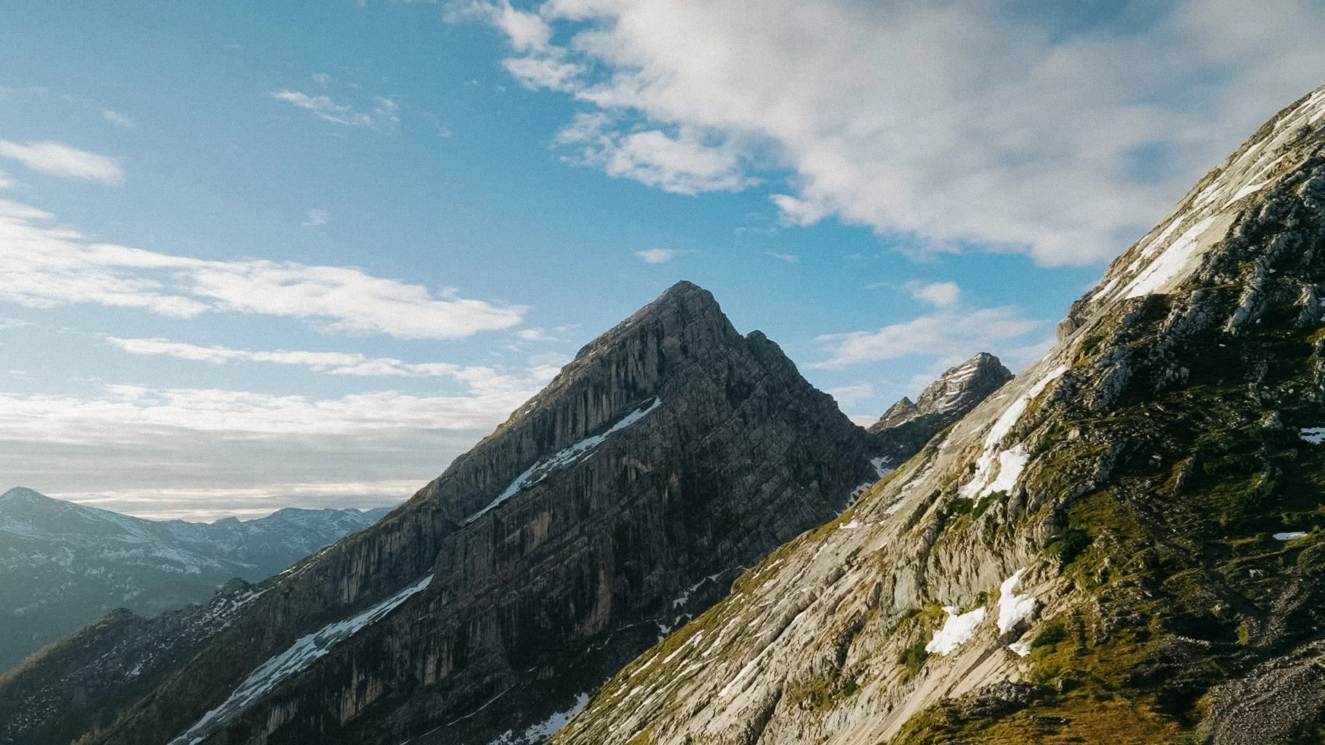 Bergformation mit schneebedeckten Pässen und bewaldeten Hängen bei bewölktem Himmel