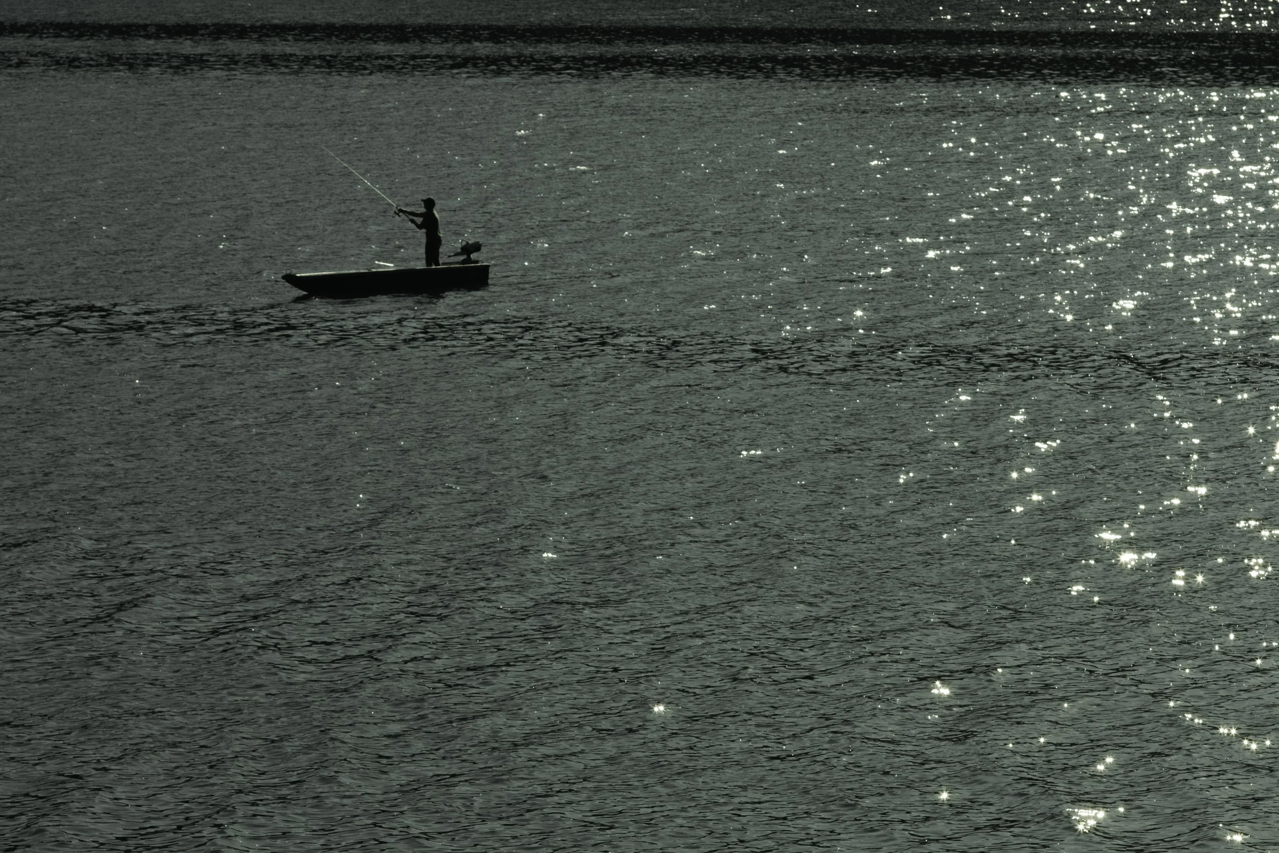 Ein Mensch steht auf einem kleinen Boot und angelt im Wasser bei Sonnenlicht.