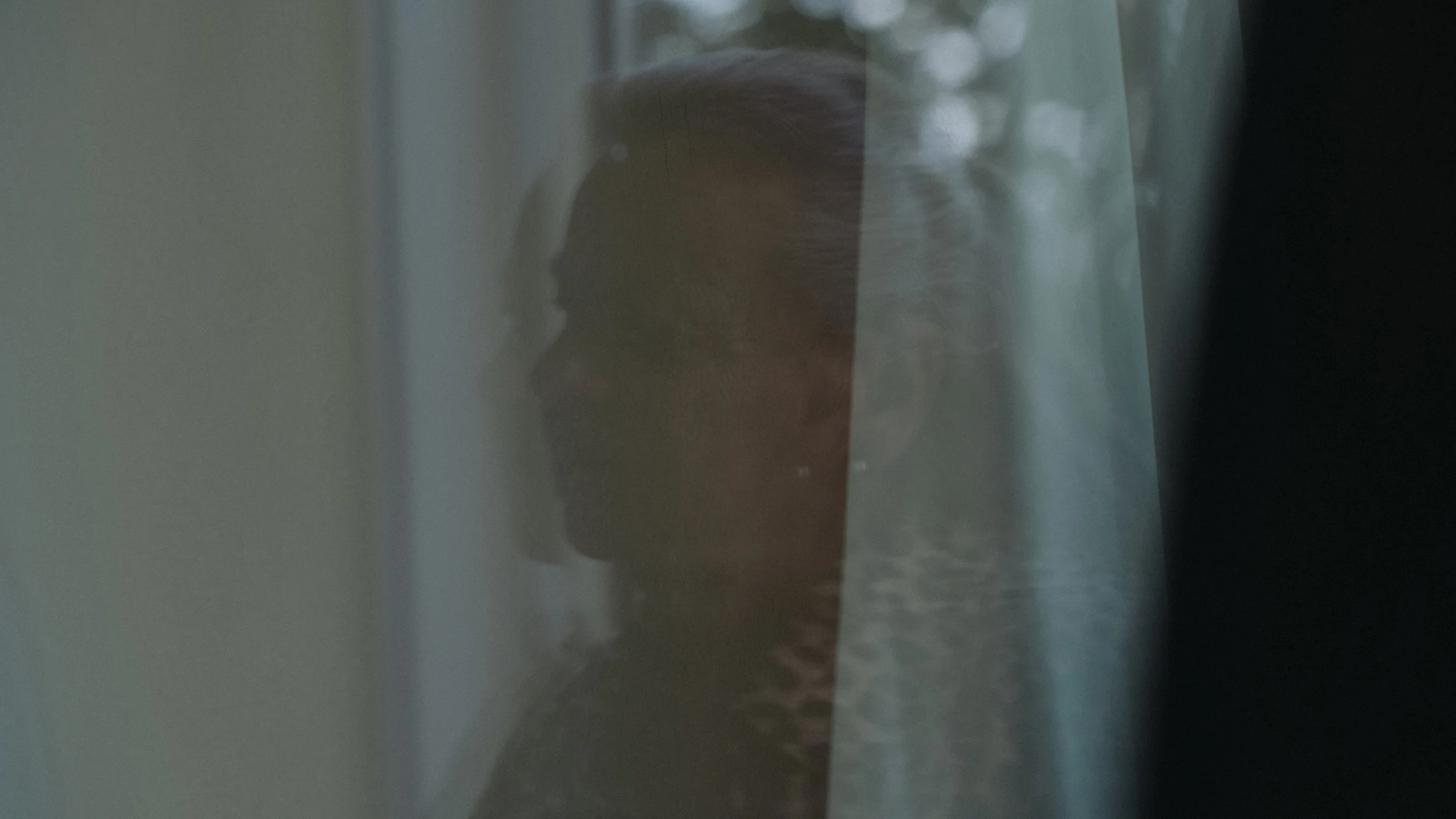 Silhouette eines Menschen, der hinter einer schimmernden Glasscheibe steht, das Gesicht ist unscharf und kaum erkennbar.