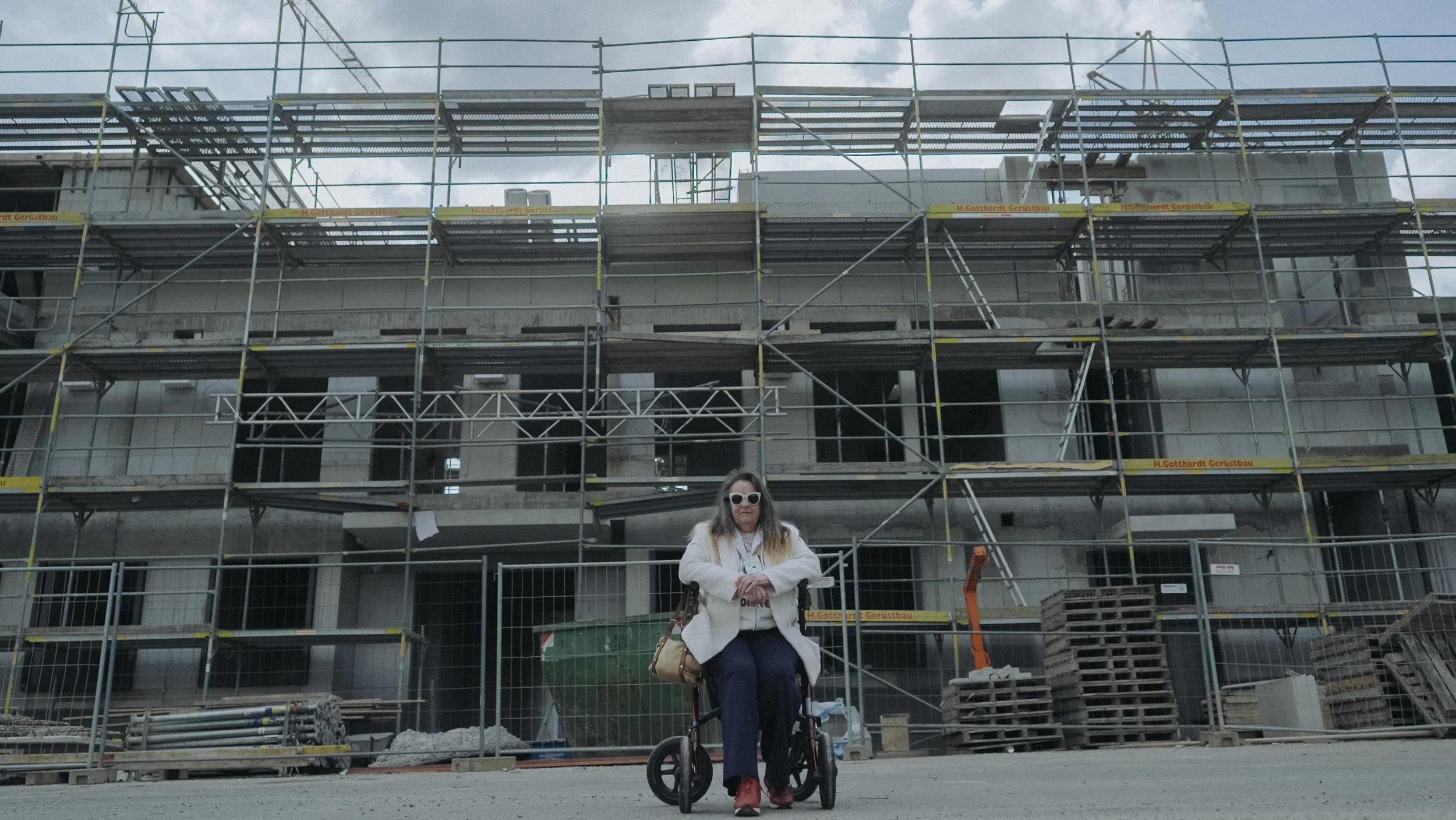 Frau in einem rollstuhl vor einem Baugerüst beim Baustellenumbau eines Gebäudes.