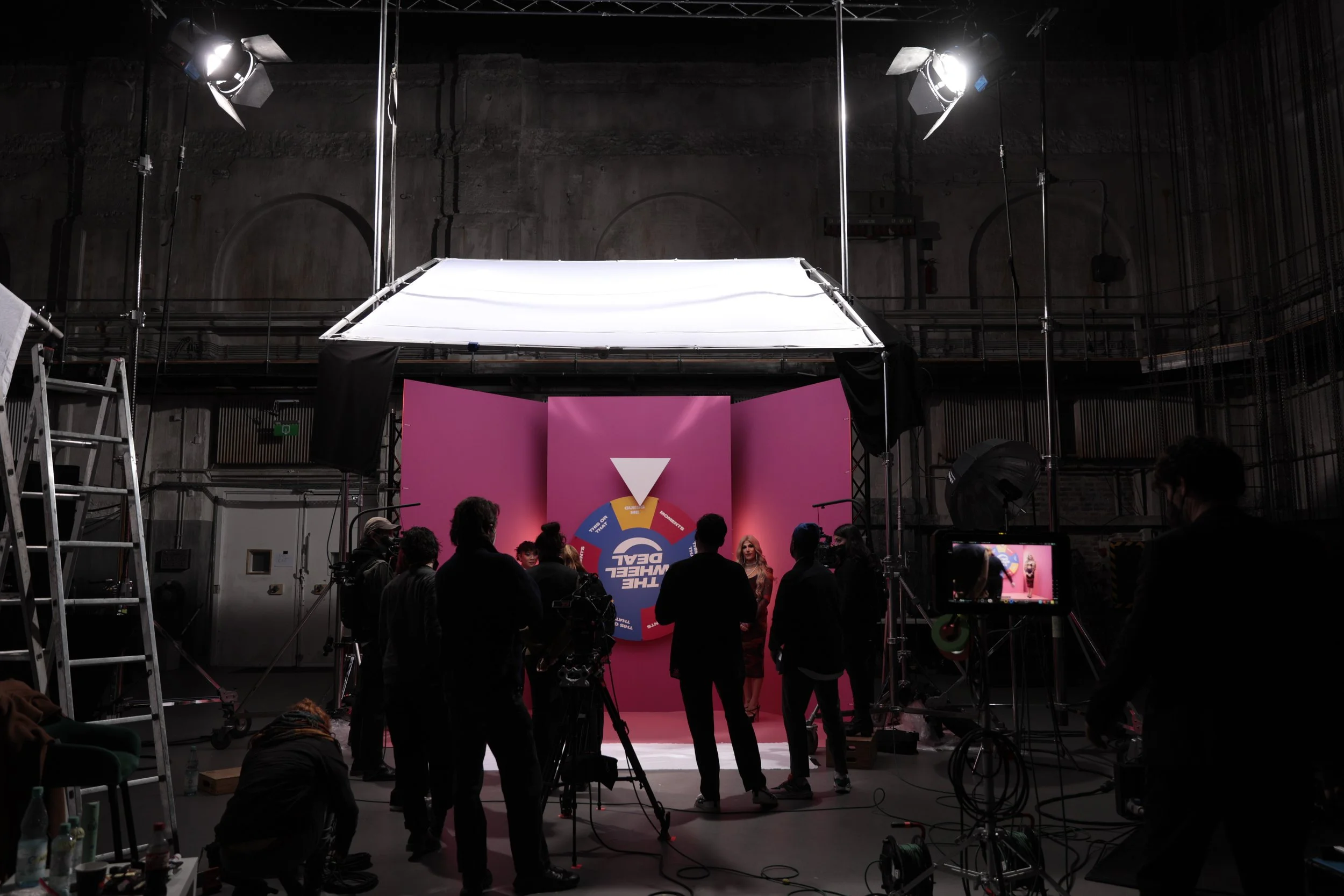 Dreh einer Fernsehsendung mit mehreren Menschen vor pinkem Hintergrund, Kamera- und Lichttechnik in einem dunklen Studio.