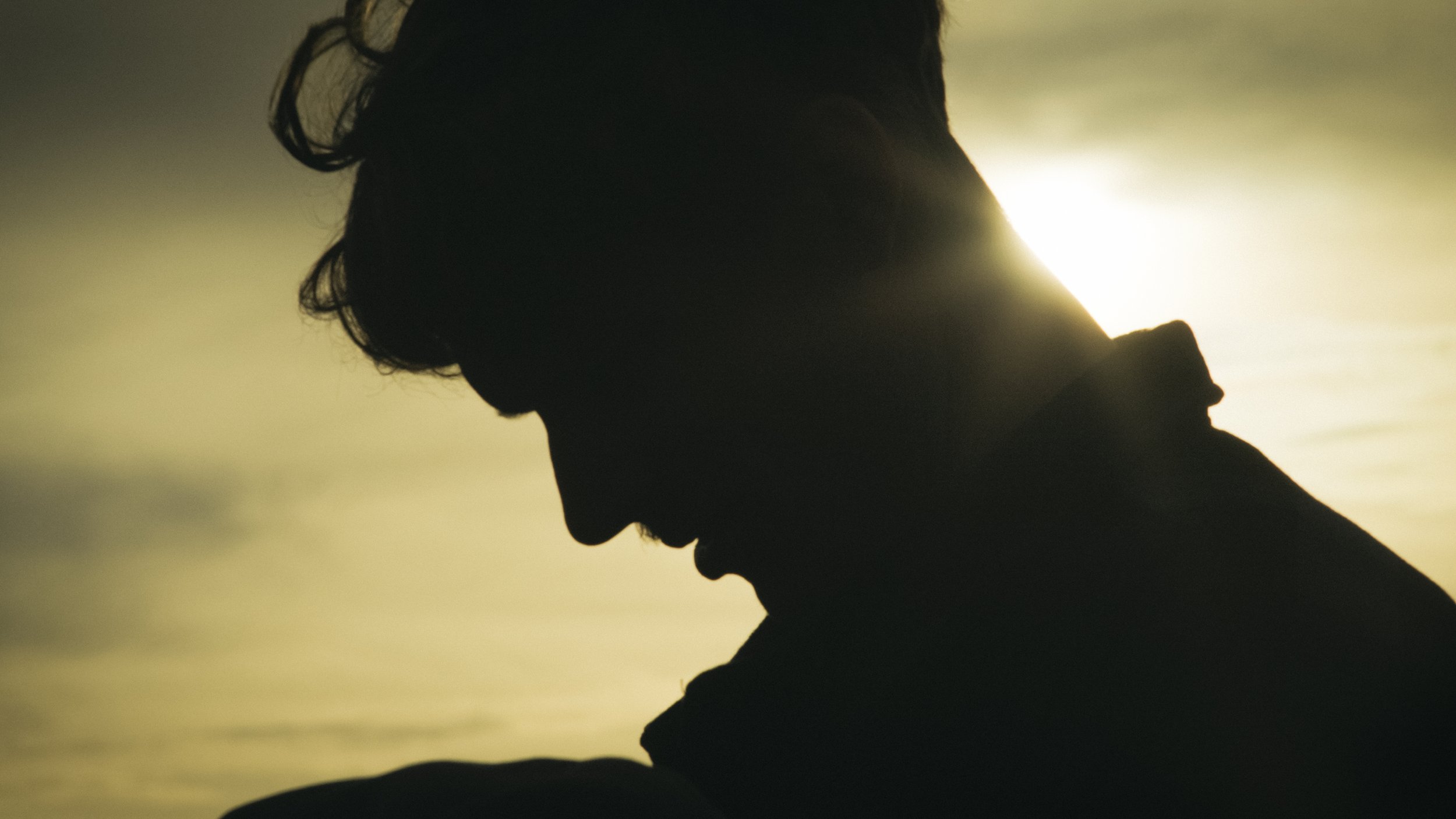 Schattenprofil eines Mannes mit nach unten geneigtem Kopf, im Hintergrund Sonnenlicht am Himmel.