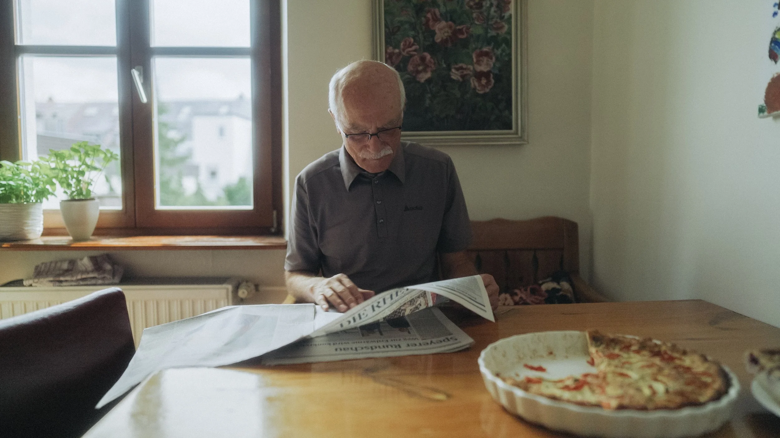 Älterer Mann liest Zeitung am Esstisch mit Pizza