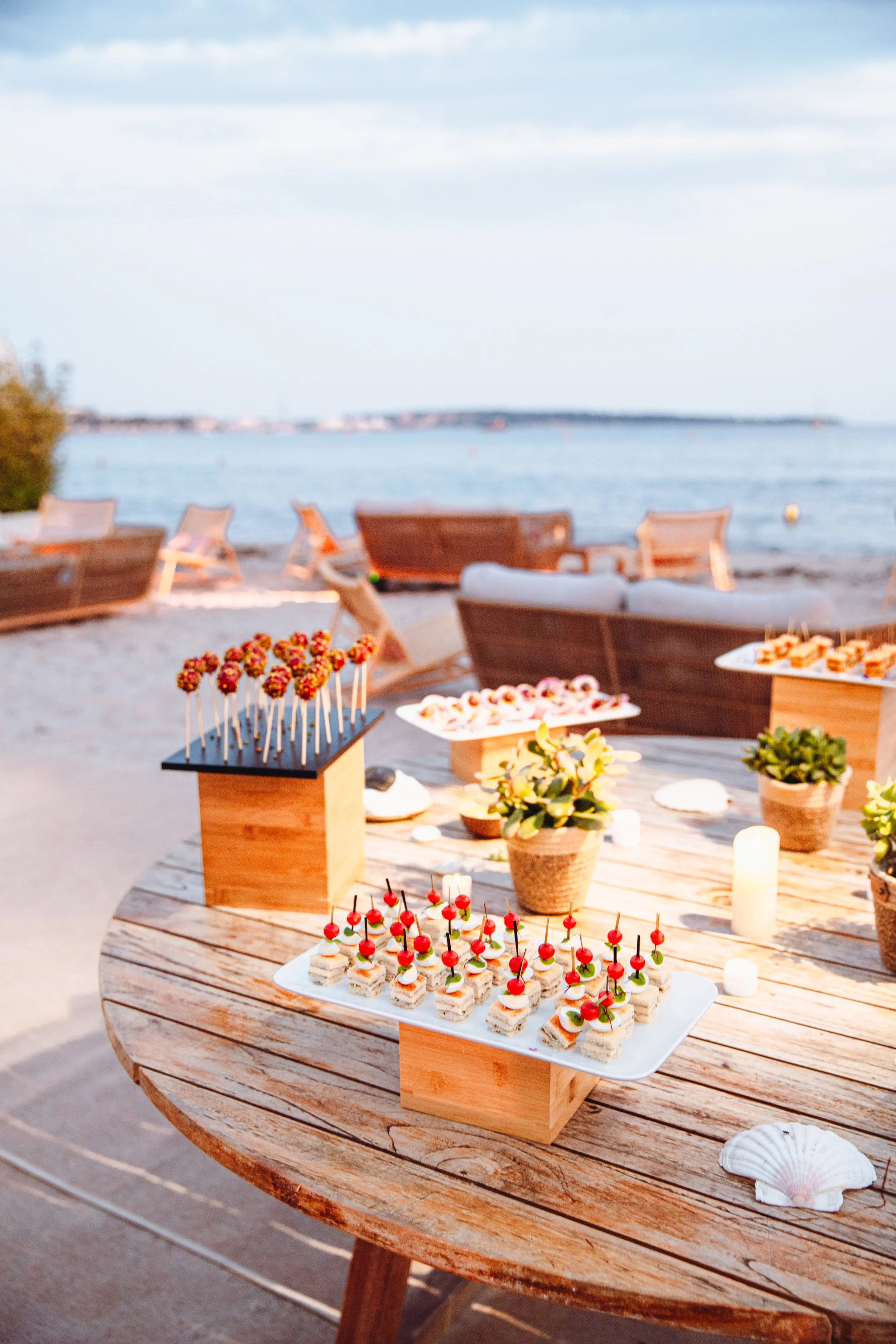 Buffet de nourriture en plein air avec des amuse-gueules sur une table en bois face à la mer, avec des chaises longues en bois à l'arrière.