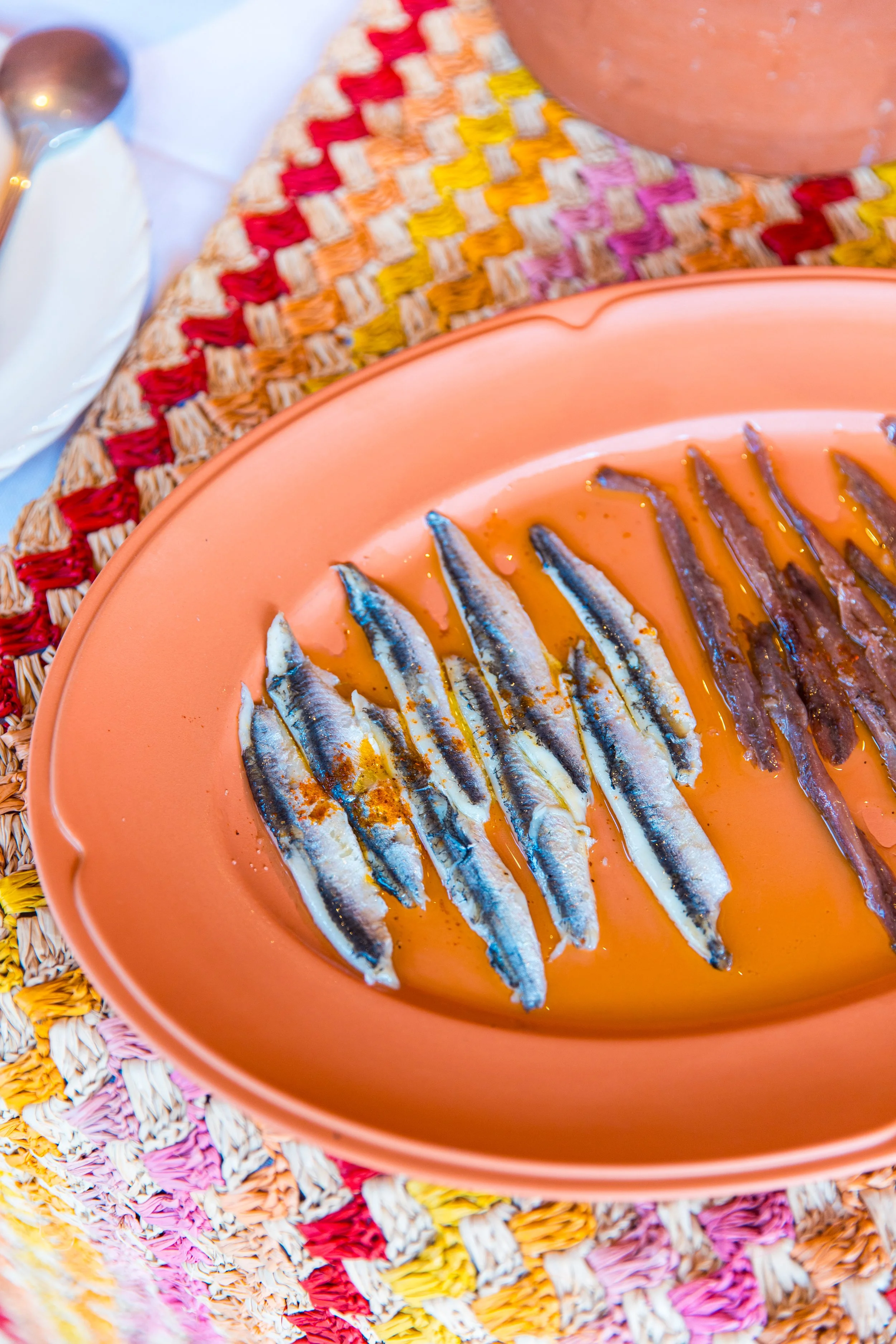 Assiette orange avec des petits poissons grillés, sur une nappe en tissu multicolore