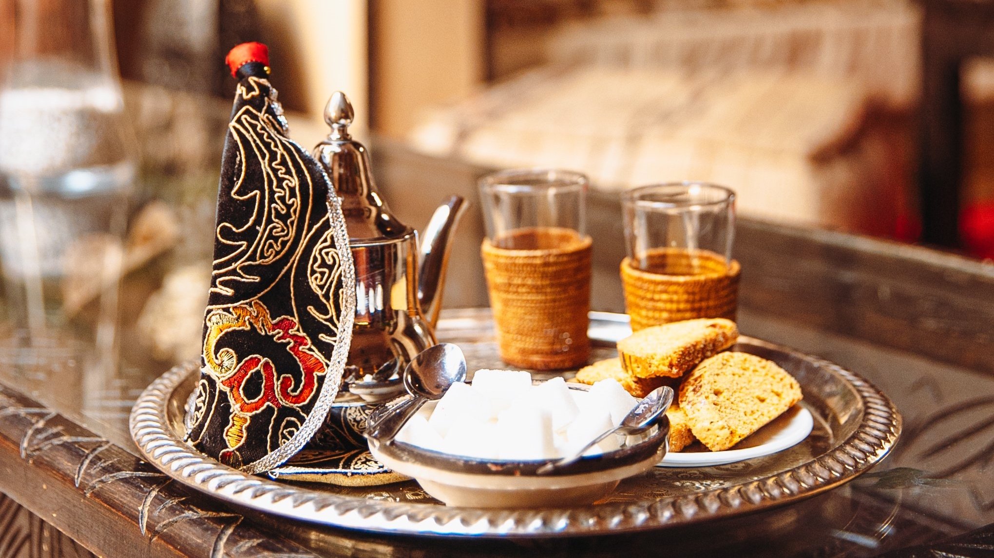 Plate de biscuits, un bol de yaourt ou de fromage blanc, une théière, deux verres remplis d'eau, une cuillère, un fer à repasser traditionnel, sur un plateau en métal, dans un décor chaleureux.