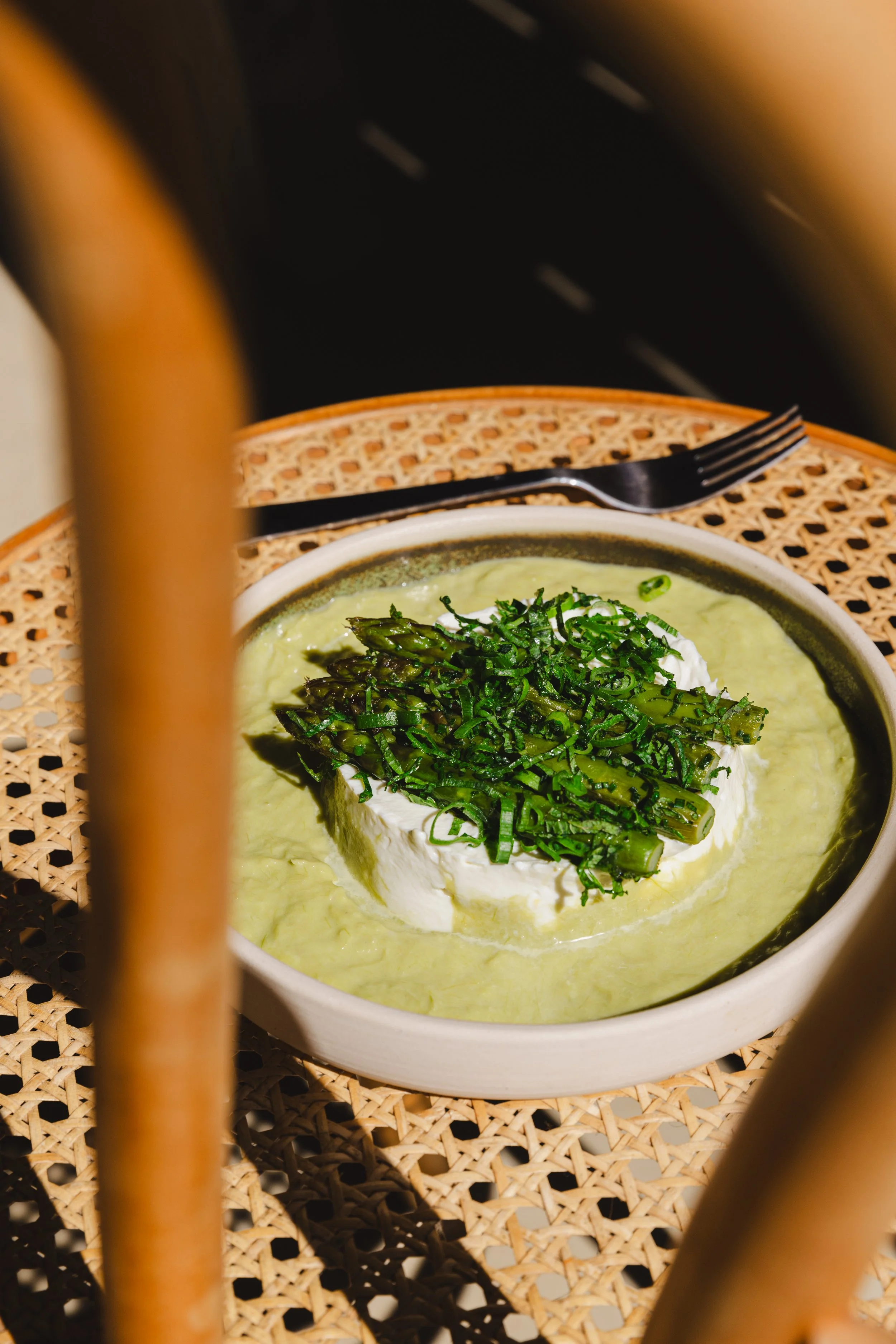 Plate de fromage vert garni de fines herbes et asperges, avec une fourchette sur une nappe en rotin.