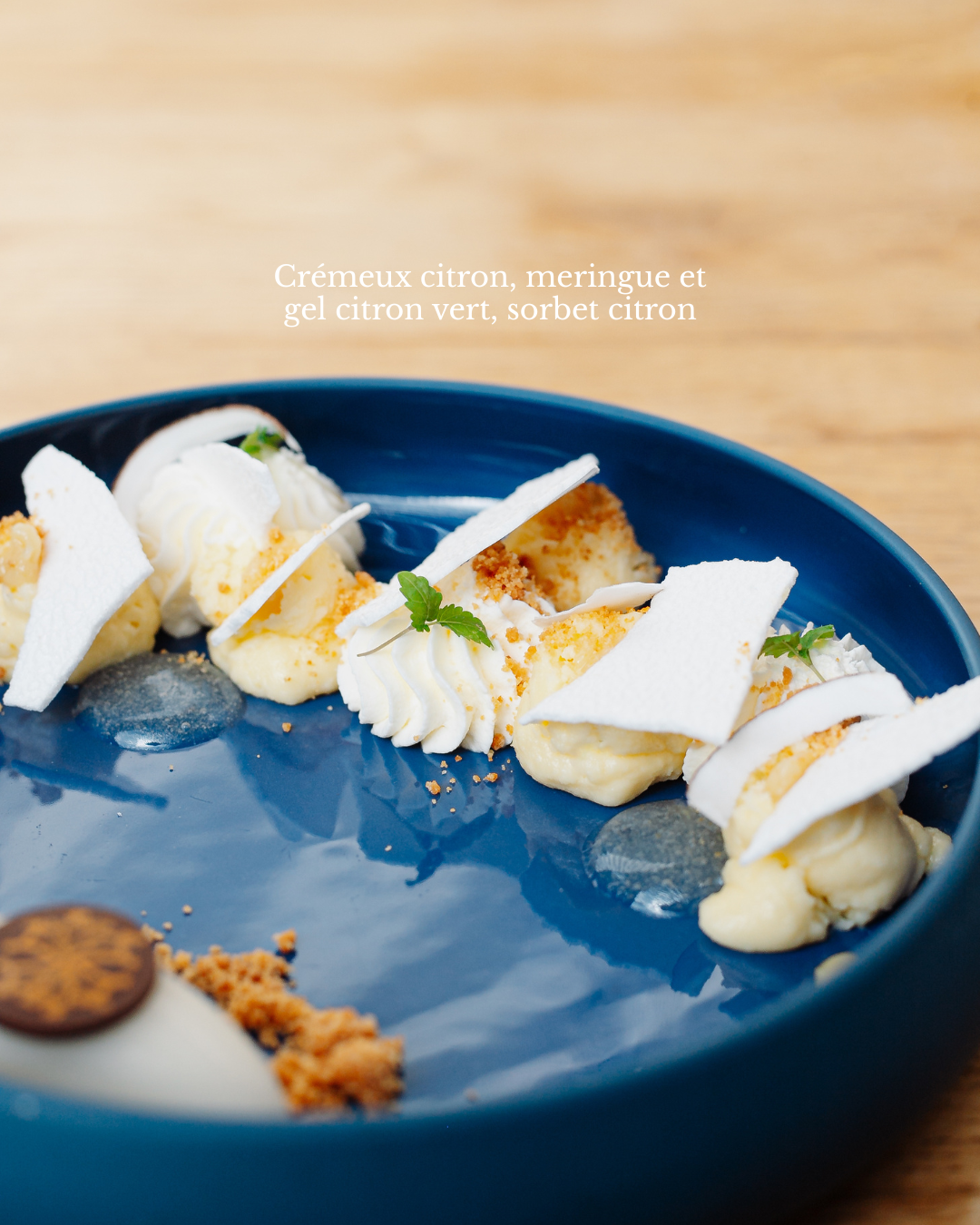 Dessert crémeux au citron avec meringue, gel de citron vert, et sorbet citron sur une assiette bleue.