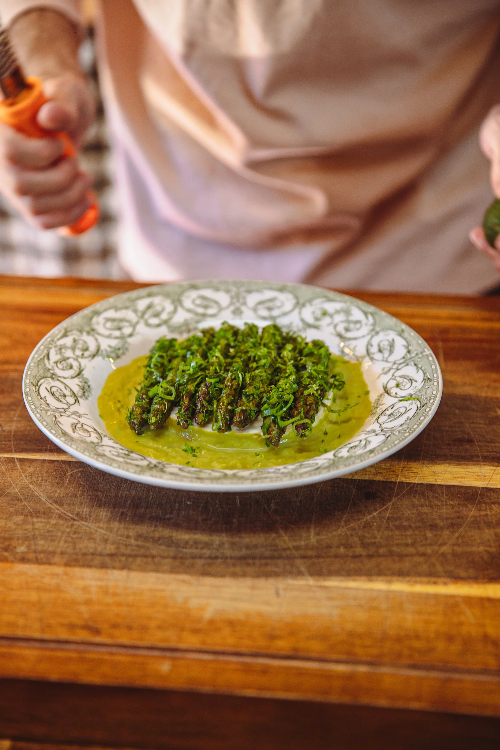 Assiette de asperges vertes piquées de ciboulette, servies avec une sauce verte, sur une table en bois.