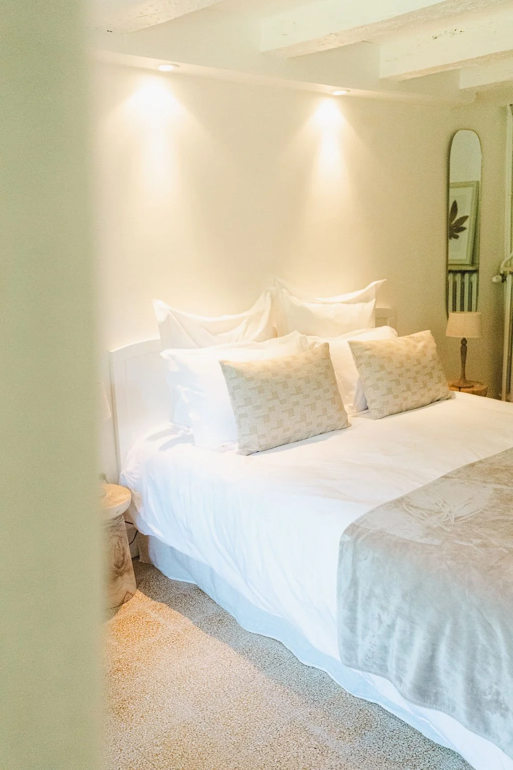 Un lit fait dans une chambre avec des coussins beige et des draps blancs, ambiance chaleureuse avec éclairage doux.
