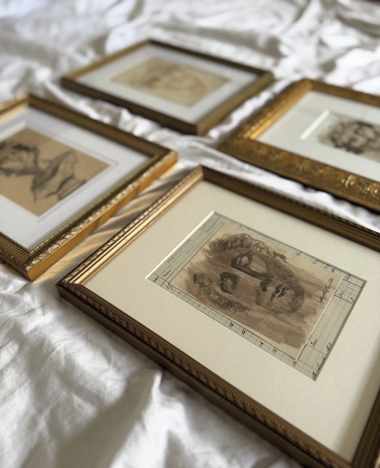 Five framed sketches or drawings, laid out on a white cloth surface.
