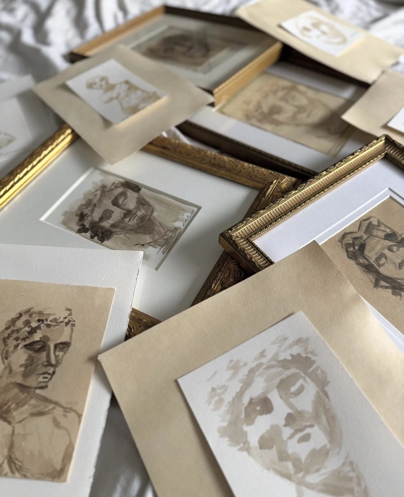 Several framed and unframed sepia-toned sketches and portraits, some in ornate gold frames, arranged on a white surface.