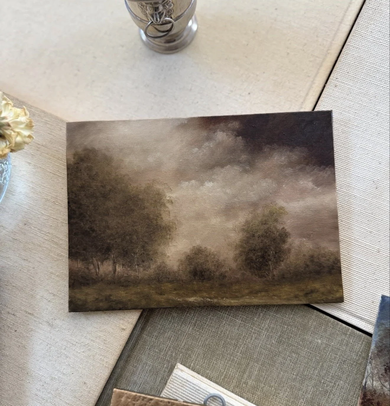 A landscape painting of trees and a cloudy sky on a table.