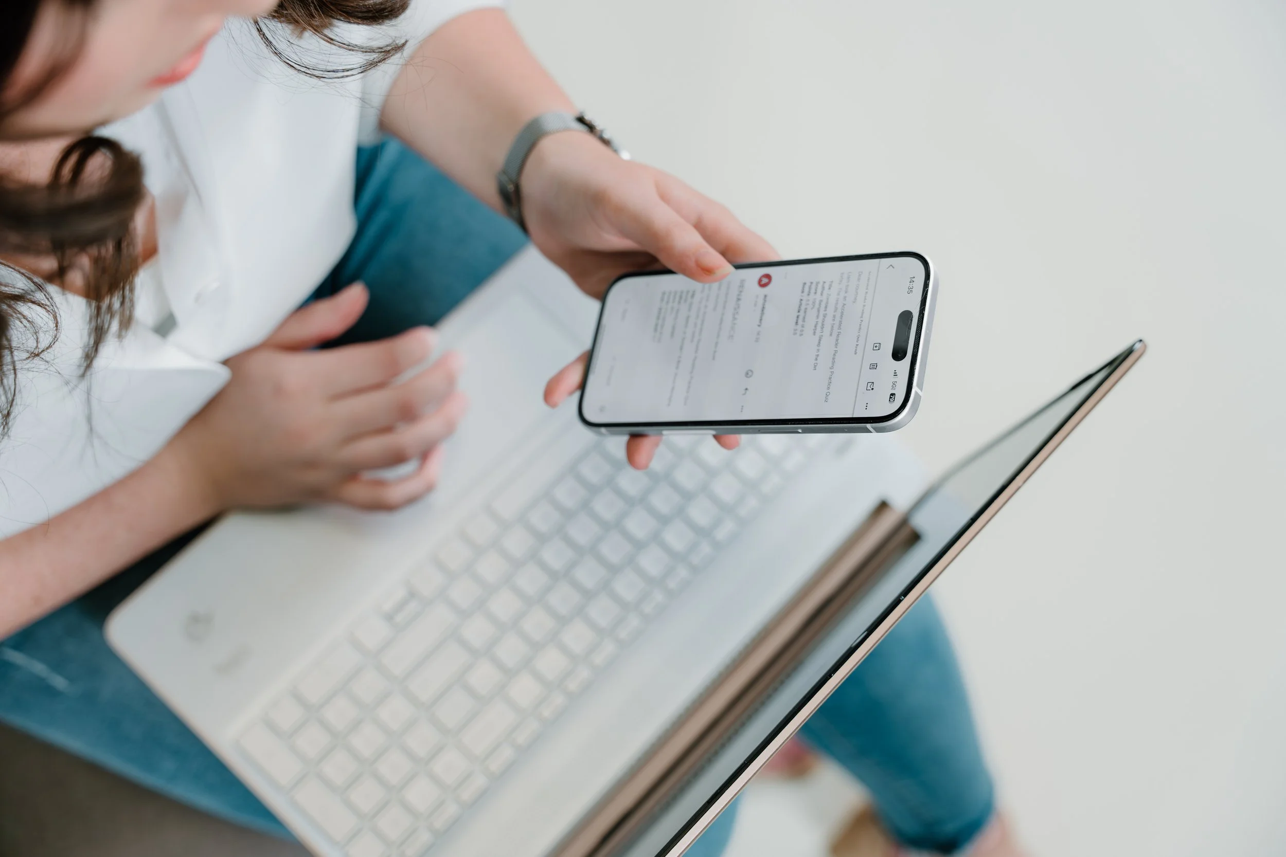 Person holding a smartphone with a message notification, sitting at a white desk with a laptop and a tablet.