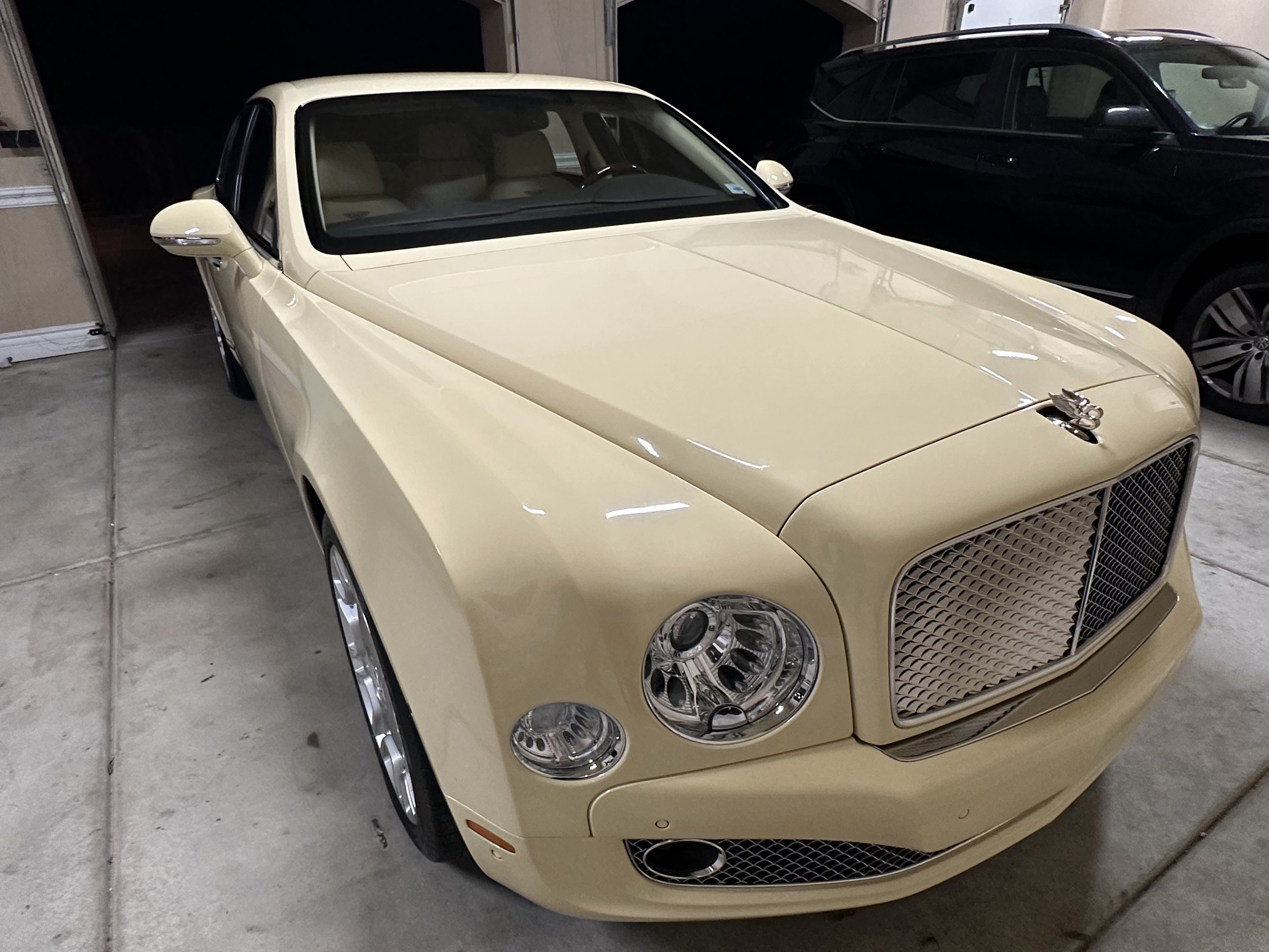 Cream-colored luxury sedan parked in a garage with another black SUV nearby.
