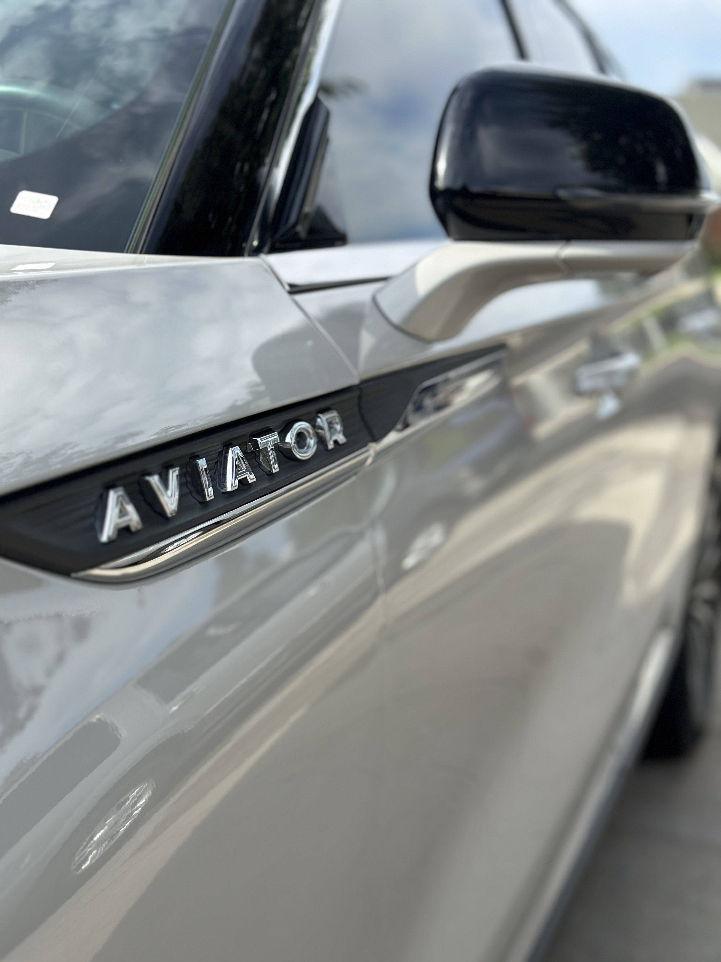Close-up of a silver vehicle's side showing the chrome 'AVIATOR' badge on the black trim beneath the side mirror.